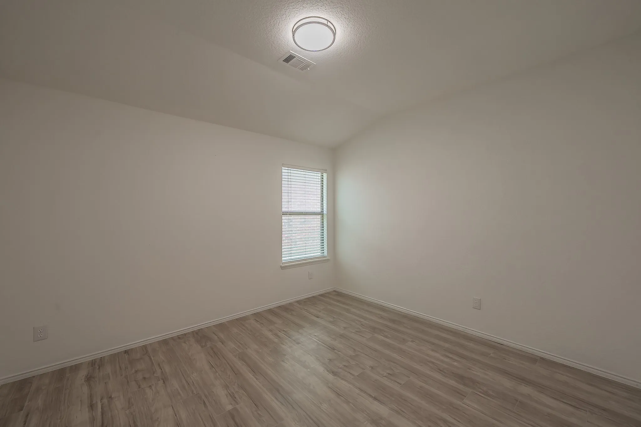 Wood-finish flooring, neutral wall tones, window with horizontal blinds, and a flush-mount ceiling light fixture