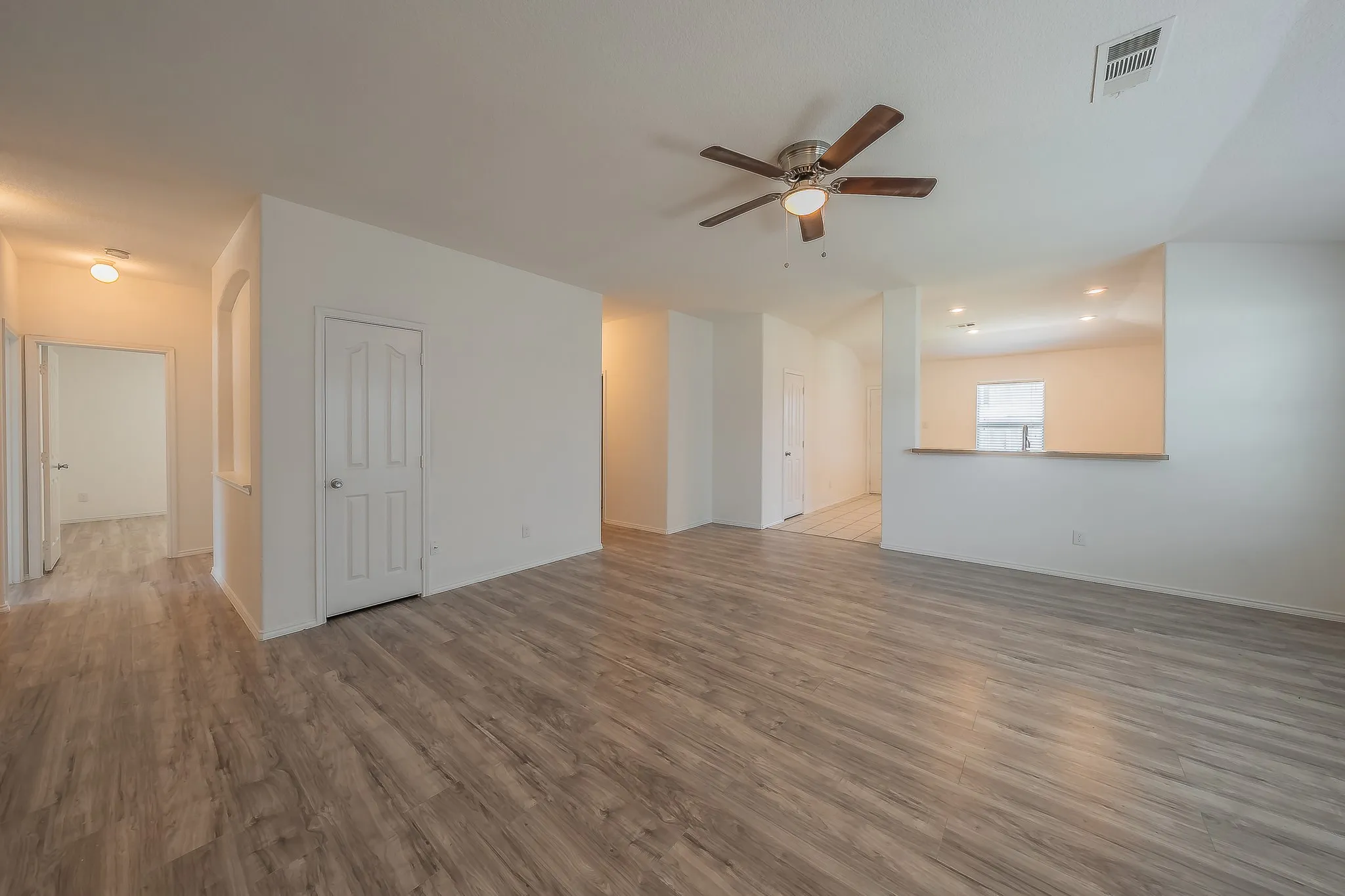 Spacious room featuring wood-finish flooring, white walls, and a ceiling fan with integrated lighting