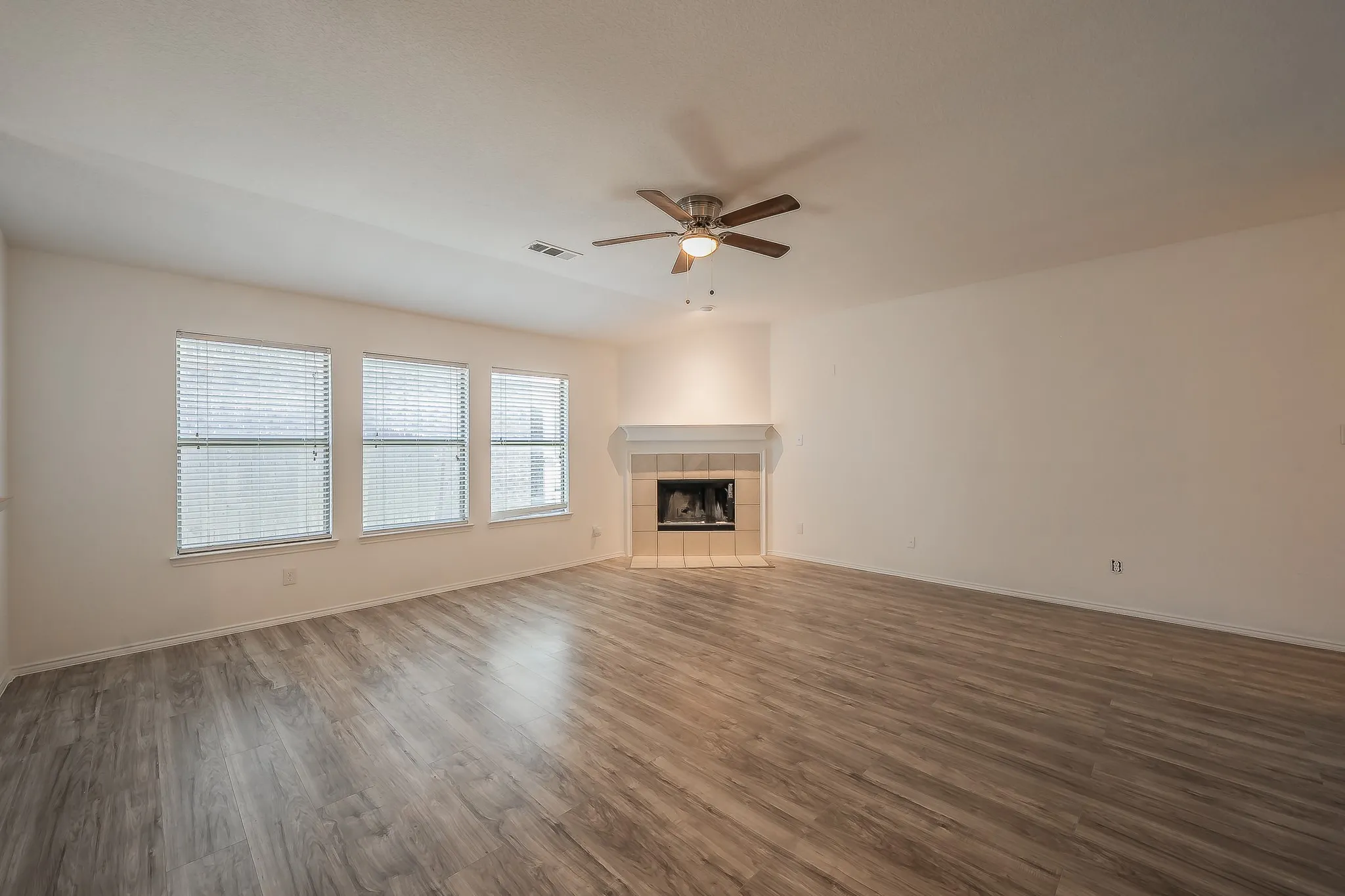 Expansive room featuring wood-finish flooring, multiple windows, a ceiling fan, and a fireplace with a mantel