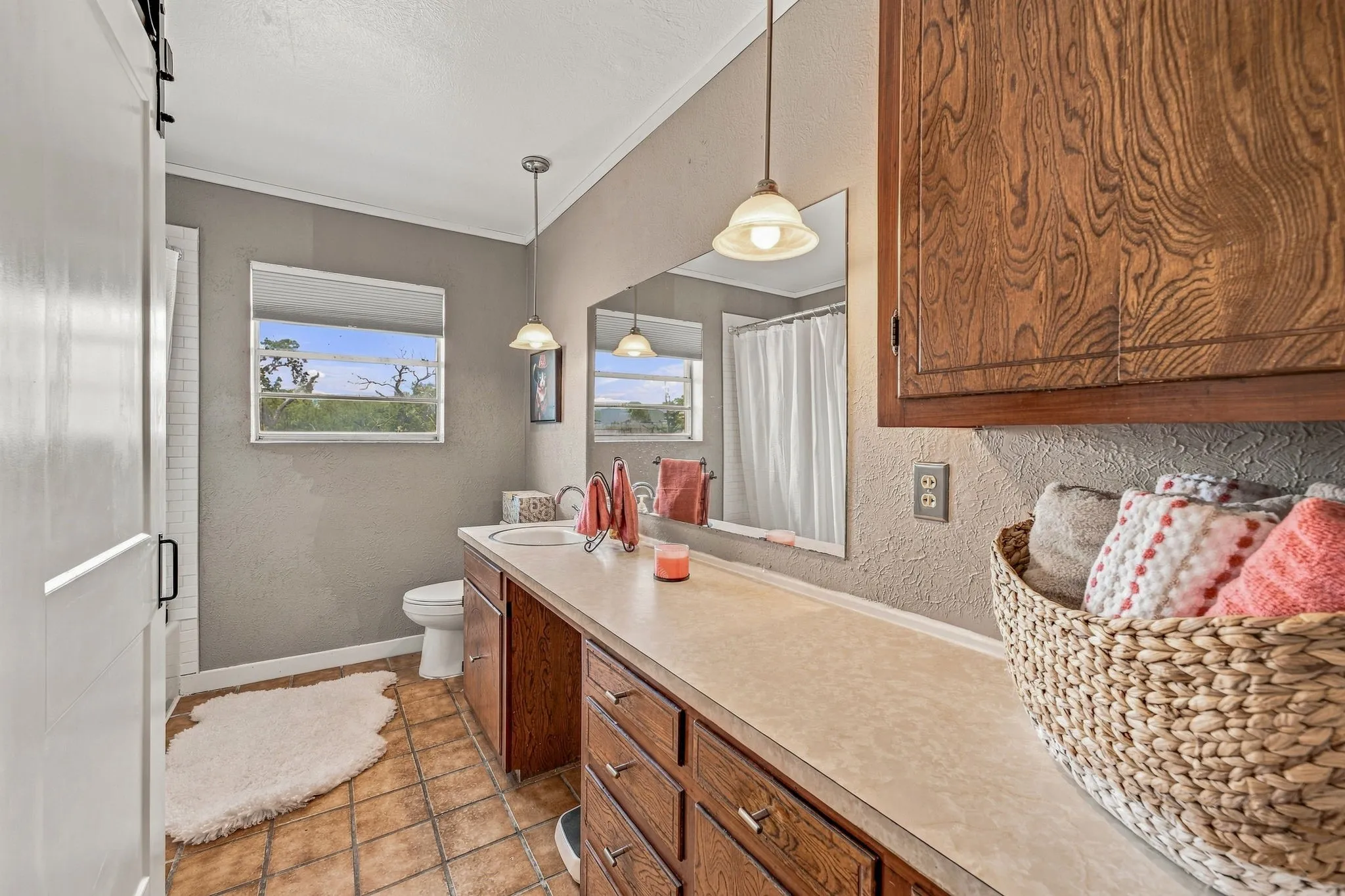 Barn door entry to bath area, dual pendant lighting, elongated vanity with integrated sink, full-width vanity mirror, and tile flooring