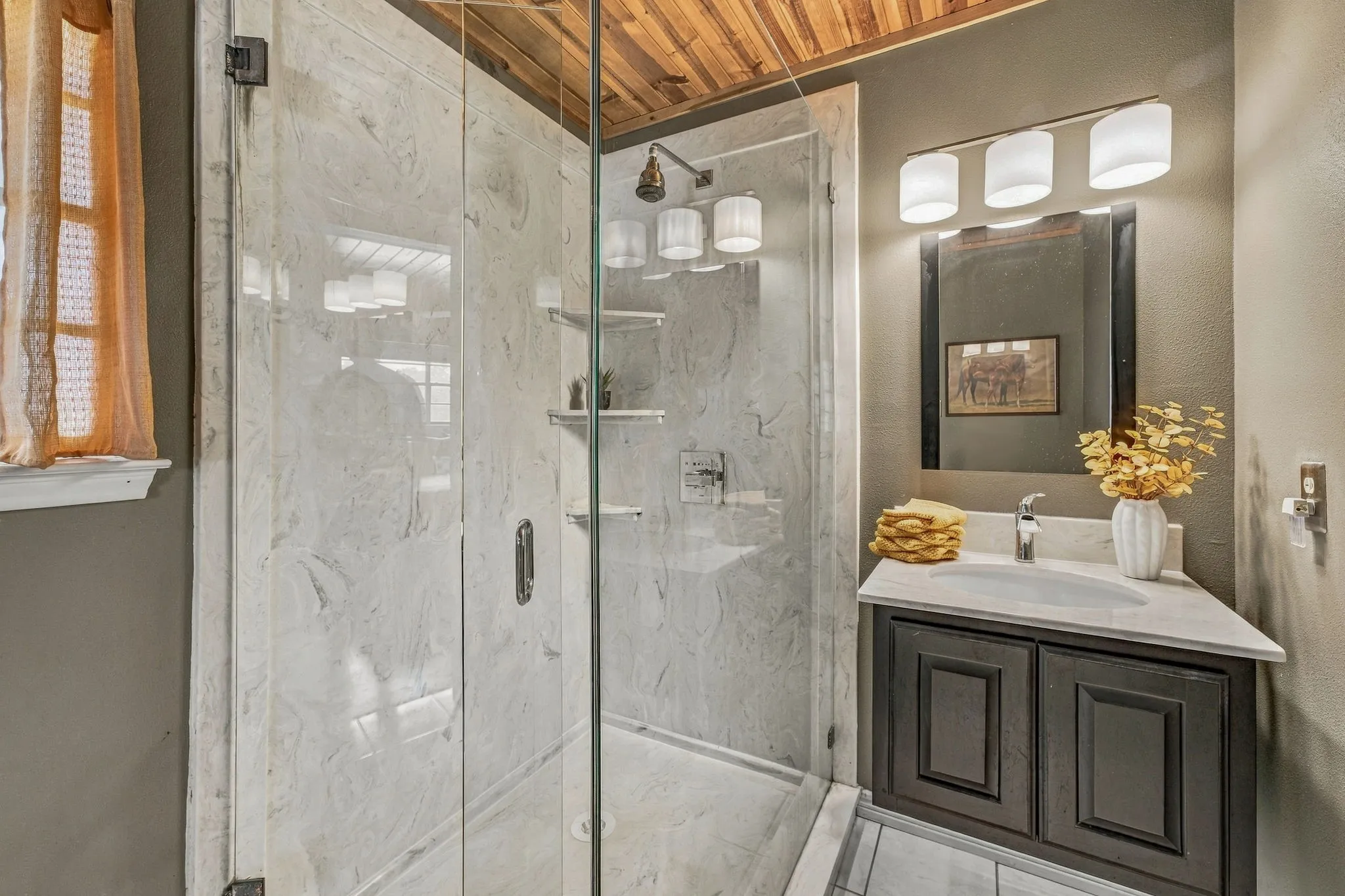 Glass-enclosed shower with stone-finish walls, wood-plank ceiling, and a single-basin vanity with a light-colored countertop