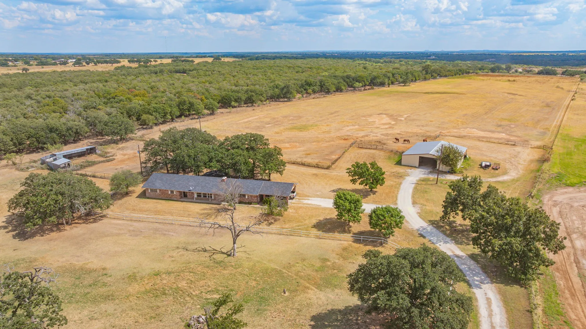 Sprawling rural property featuring a single-story residence situated on expansive acreage with mature tree clusters, improved pastureland, and a secondary outbuilding