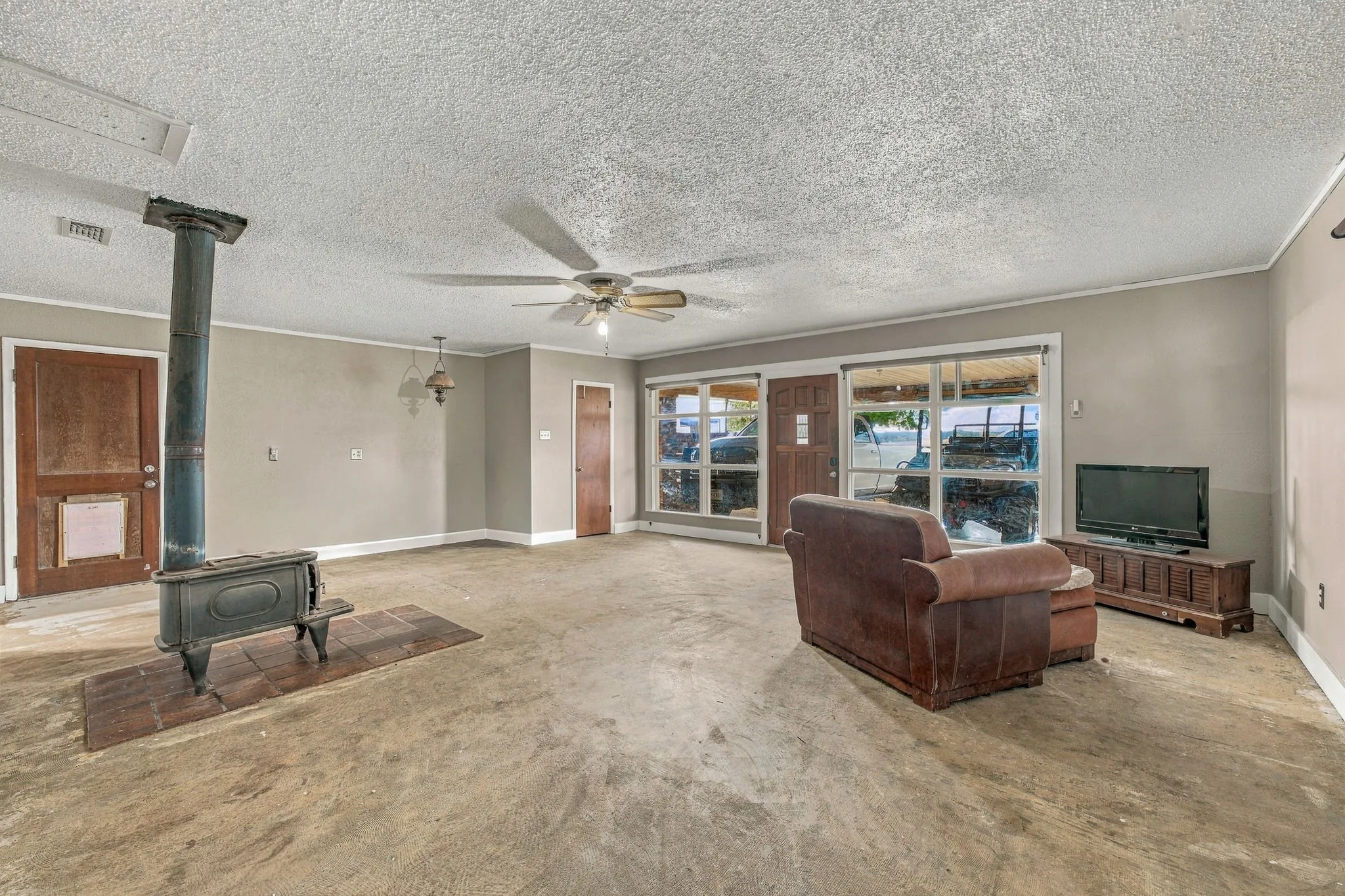 Wood-burning stove on a brick-tile hearth, large windows, multiple wood panel doors, and a ceiling fan