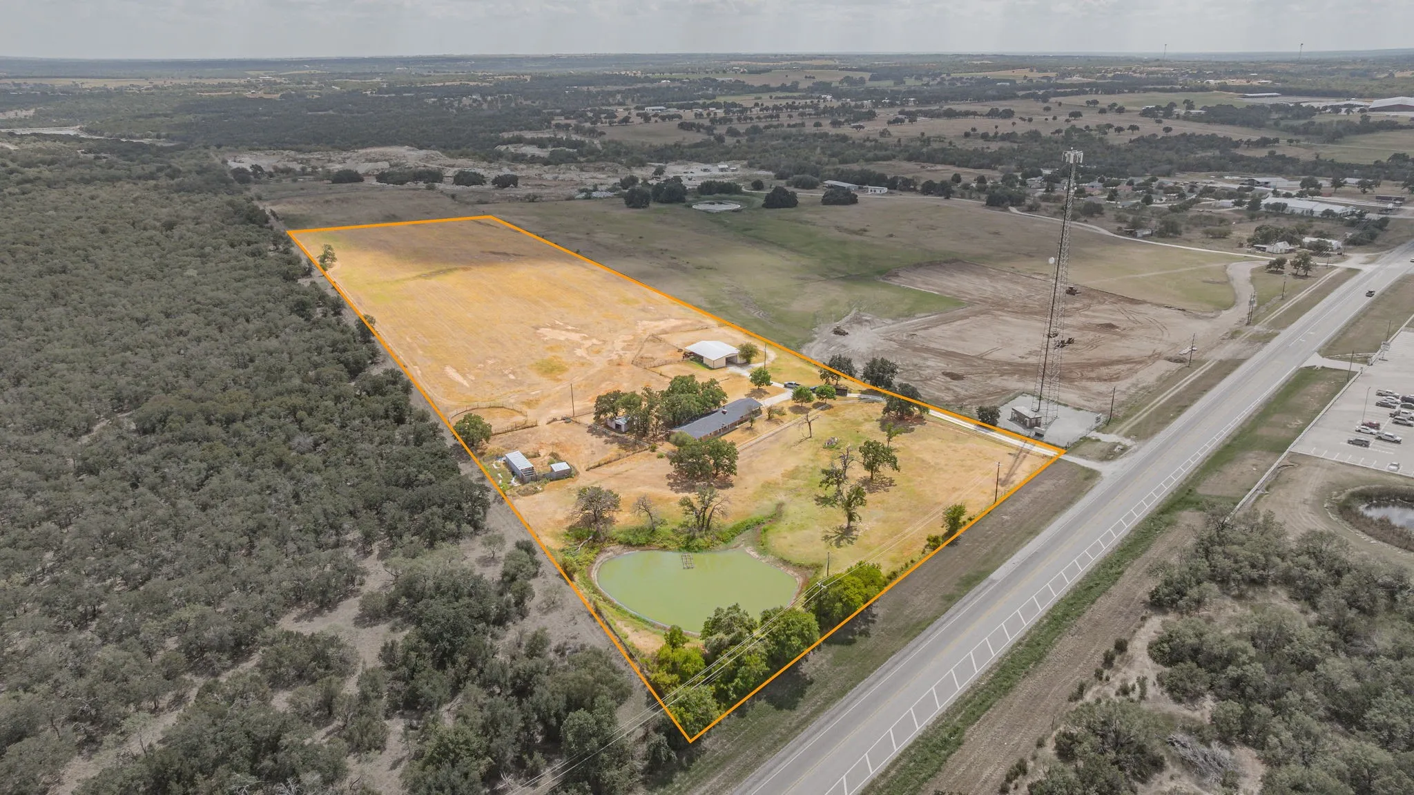 Expansive property featuring a large open field, multiple structures, mature trees, a private pond, and direct road frontage