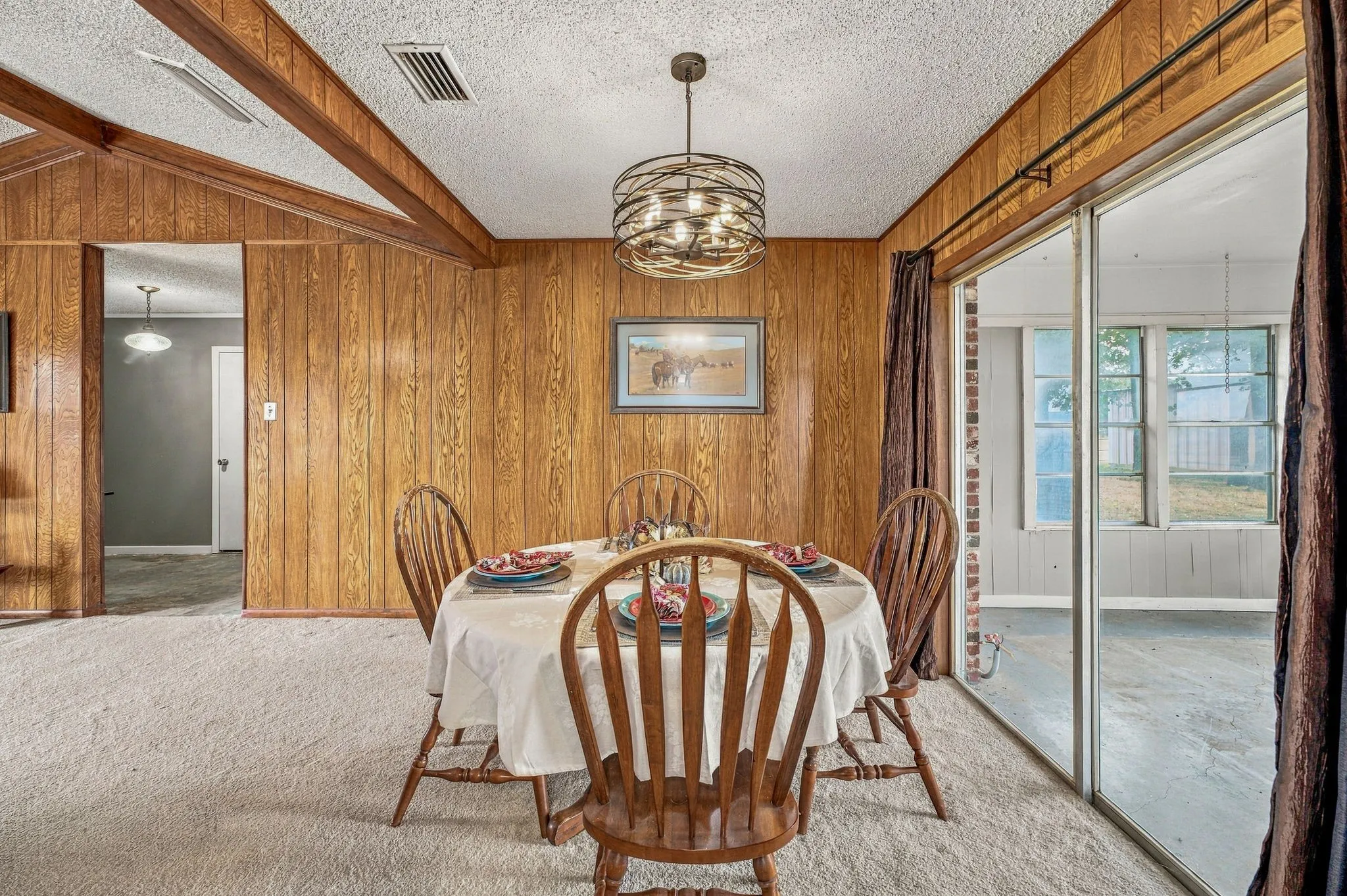 Dining area featuring wood-paneled walls, vaulted ceiling with exposed wood beams, and a contemporary spherical chandelier