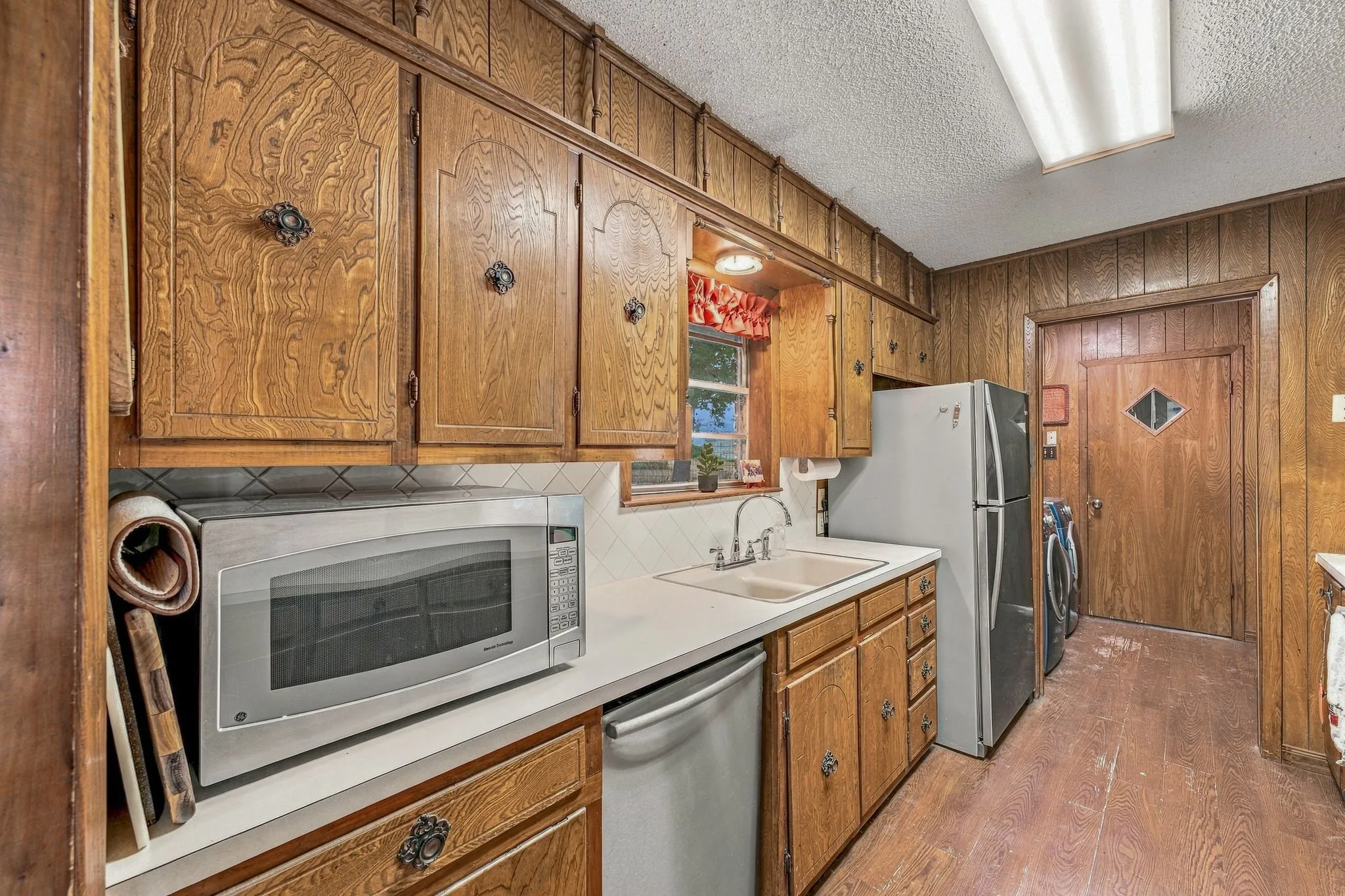 Wood-paneled walls and cabinetry, white solid-surface countertops, and a double-basin sink with a chrome faucet