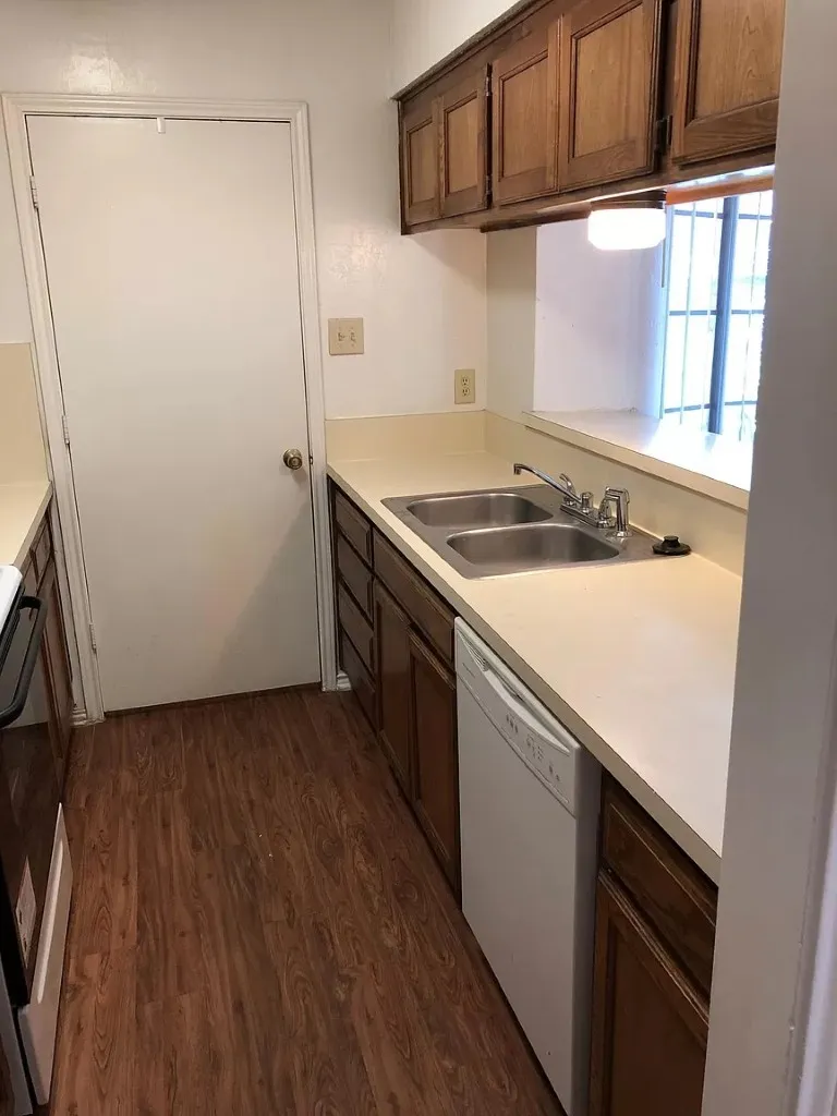 Kitchen featuring wood-finish flooring, wood cabinetry, a dual basin stainless steel sink, and a white dishwasher
