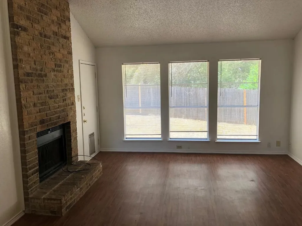 Brown brick fireplace with a raised hearth, wood-finish flooring, and multiple windows