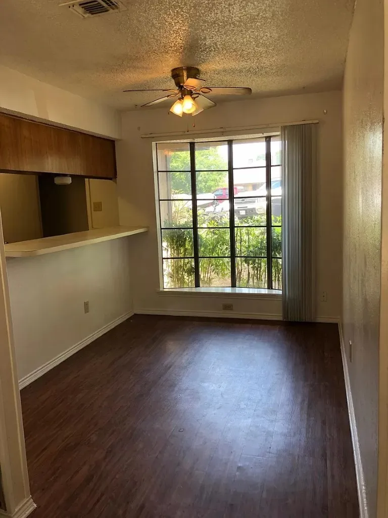 Wood-finish flooring throughout, a large window with vertical blinds, and a brass-finish ceiling fan with integrated lighting