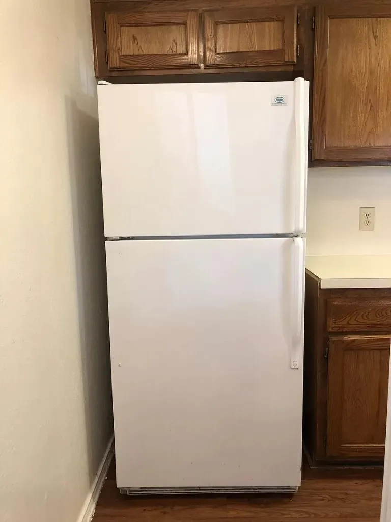 White top-freezer refrigerator with wood-finish upper cabinetry, wood-finish base cabinetry, and light-toned countertops