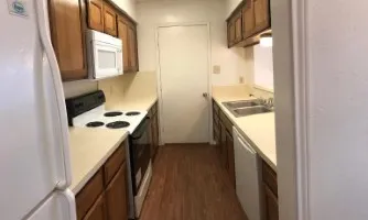 Galley kitchen featuring wood-finish flooring, white appliances, laminate countertops, and wood cabinetry