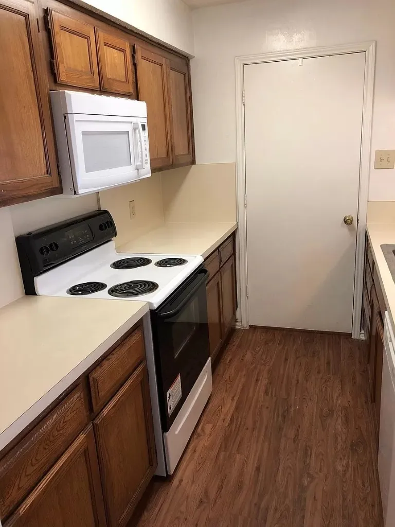 Kitchen featuring wood-finish flooring, wood cabinetry, light-toned countertops, white electric range, and a built-in microwave