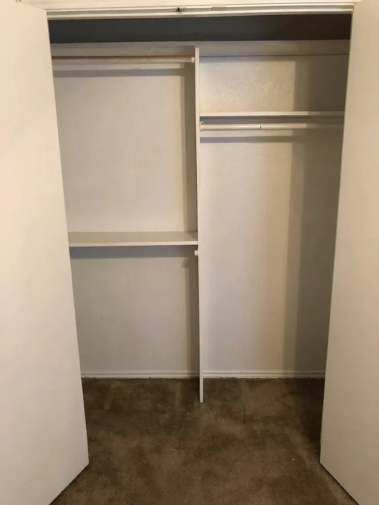 Built-in closet system with multiple shelves and hanging rods, set against light-colored walls and carpet flooring