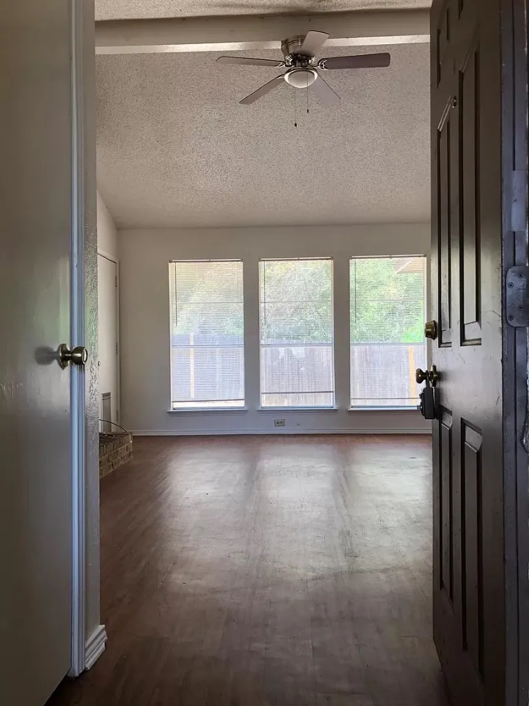 Wood-finish flooring, vaulted ceiling, ceiling fan with integrated lighting, three windows with blinds, and a brick hearth