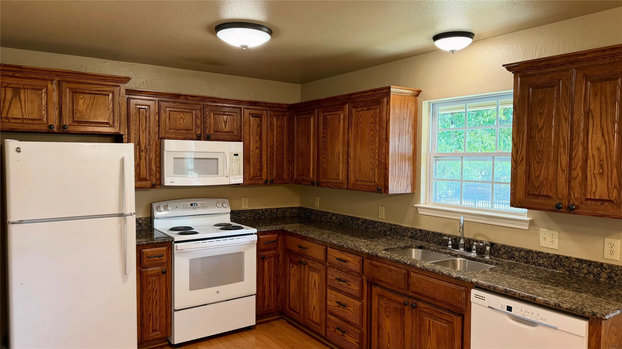Kitchen featuring wood-finish cabinetry, white appliances, and dark speckled countertops