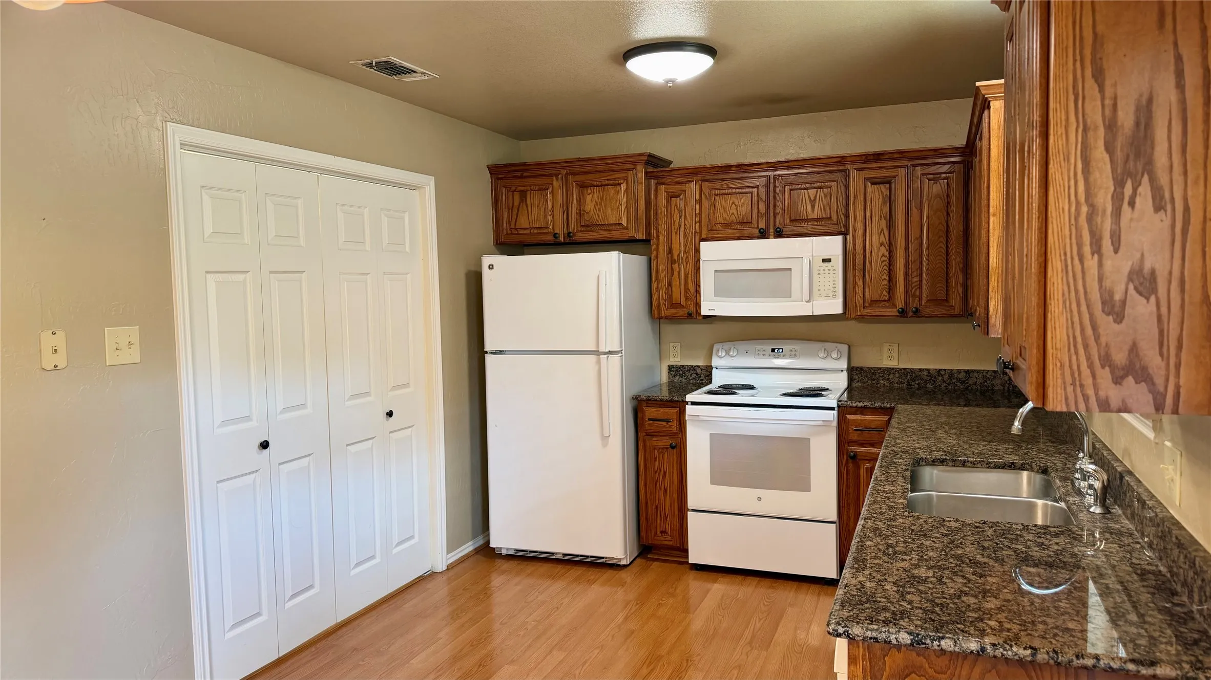 Kitchen featuring wood-finish flooring, wood cabinetry, granite-style countertops, and white appliances