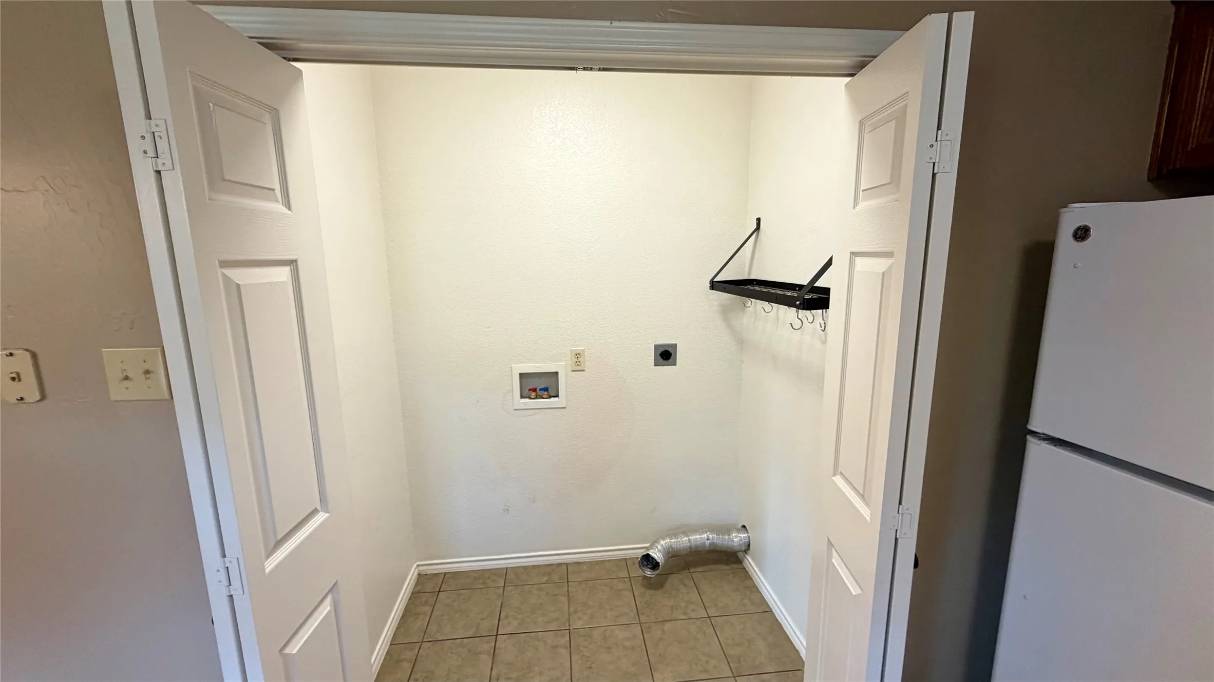 Laundry area featuring tile flooring, bi-fold panel doors, and wall-mounted shelving