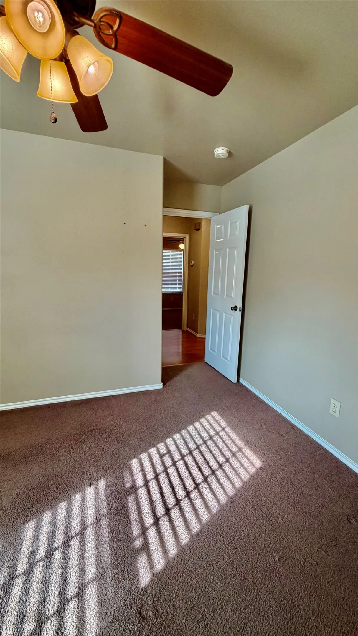 Ceiling fan with integrated lighting, neutral wall paint, white interior door, brown carpeting, and a smoke detector