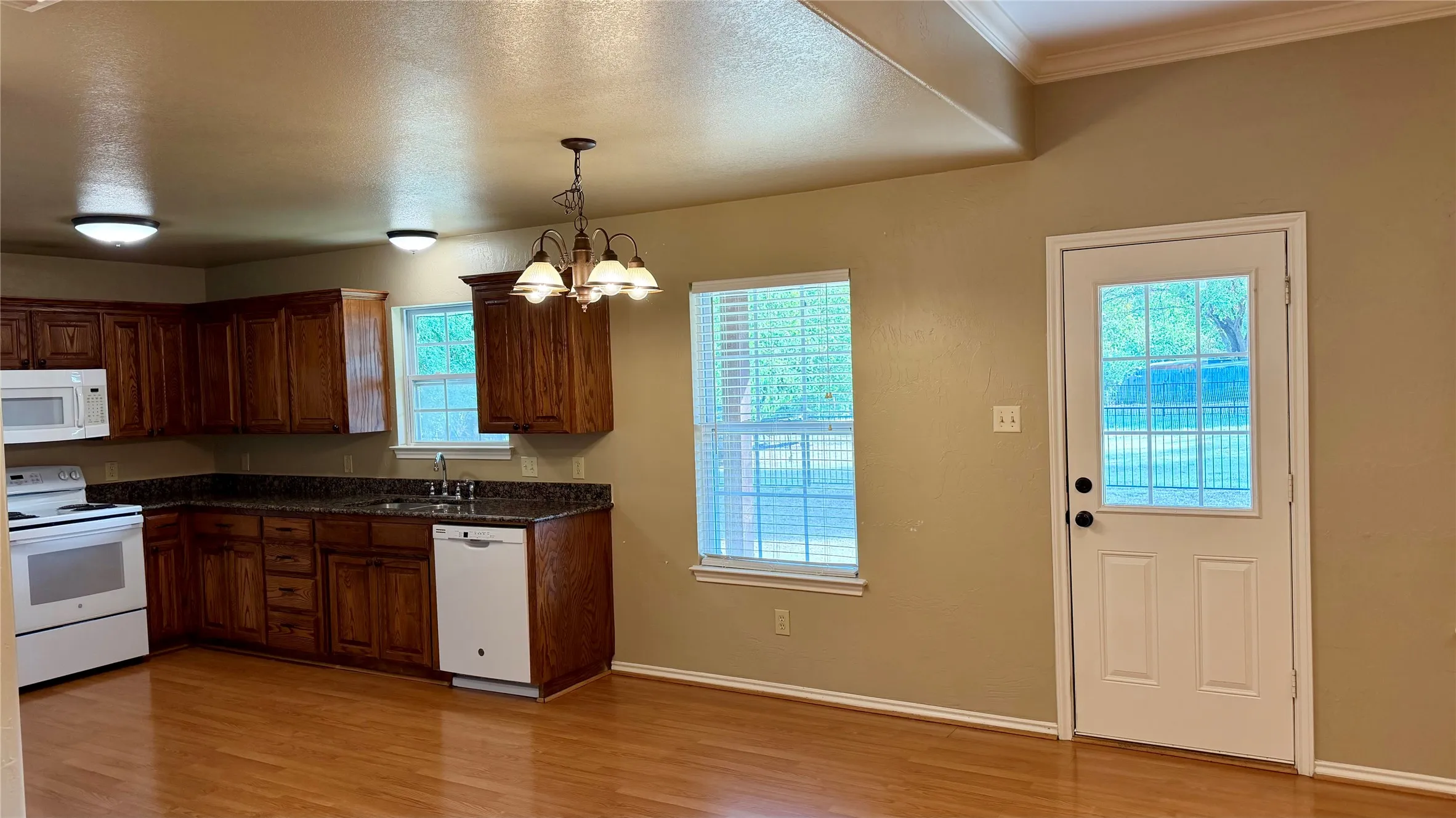 Kitchen featuring wood-finish flooring, wood cabinetry, dark countertops, and white appliances