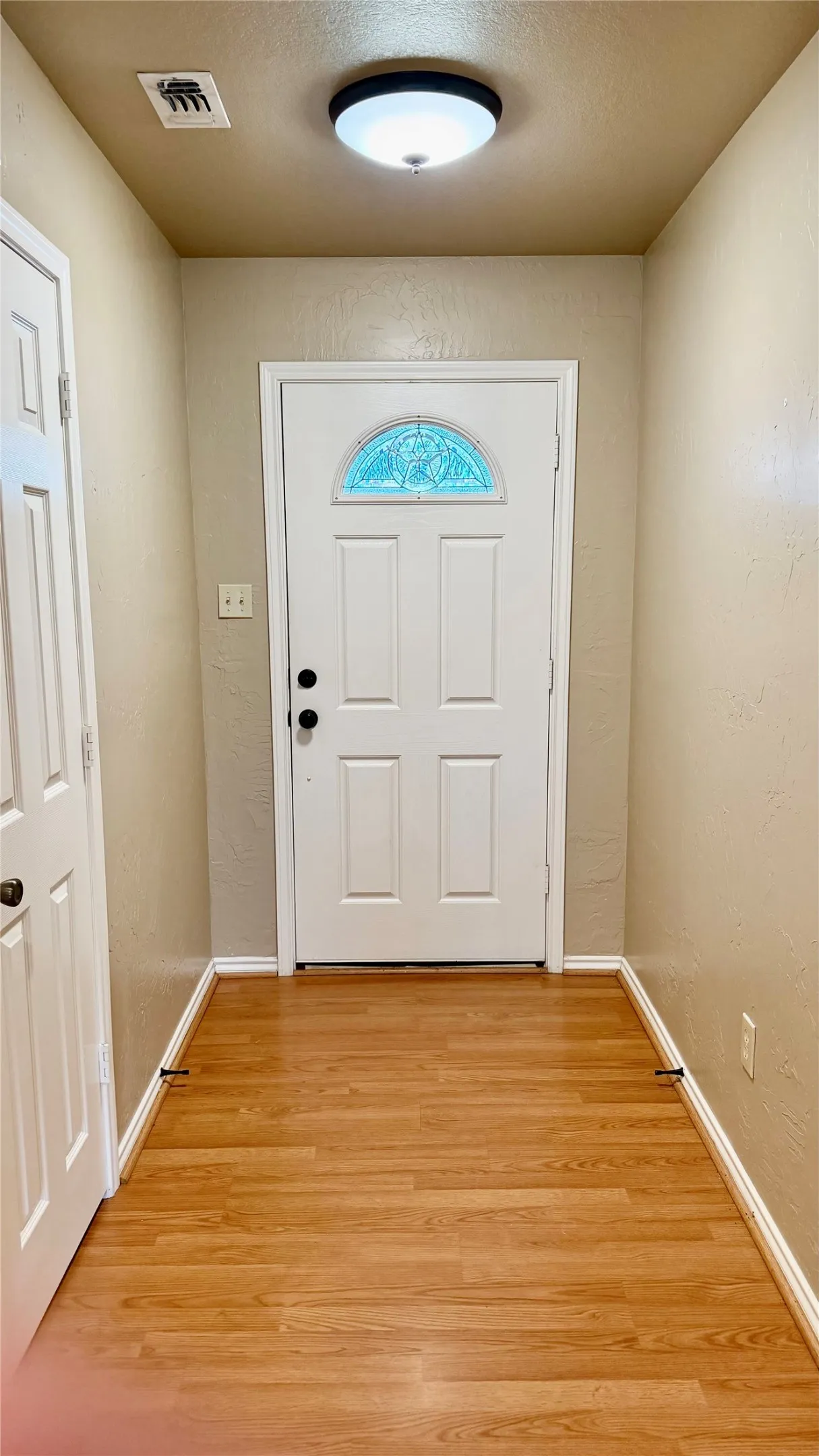 Wood-finish flooring with a white paneled door featuring a decorative transom