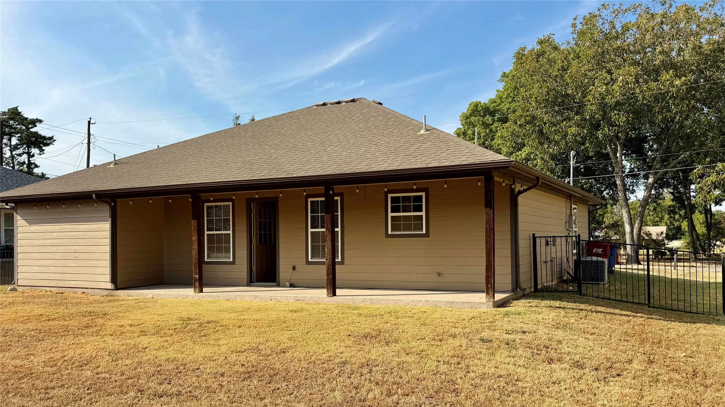 Covered patio with wood-finish support columns, a shingled roof, and tan siding