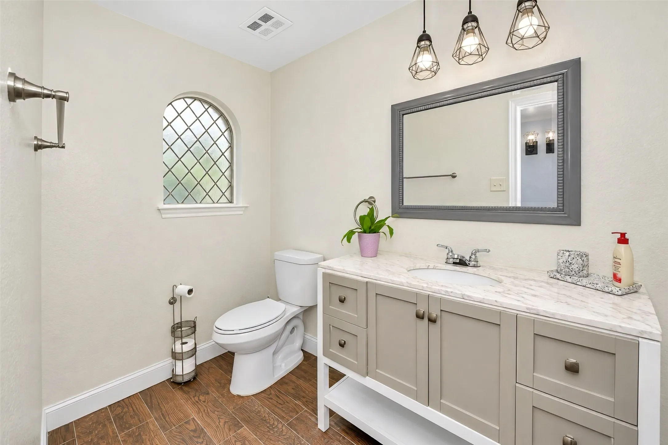 Arch-top leaded glass window, wood-finish flooring, vanity with stone countertop, vessel sink, and industrial-style pendant lighting