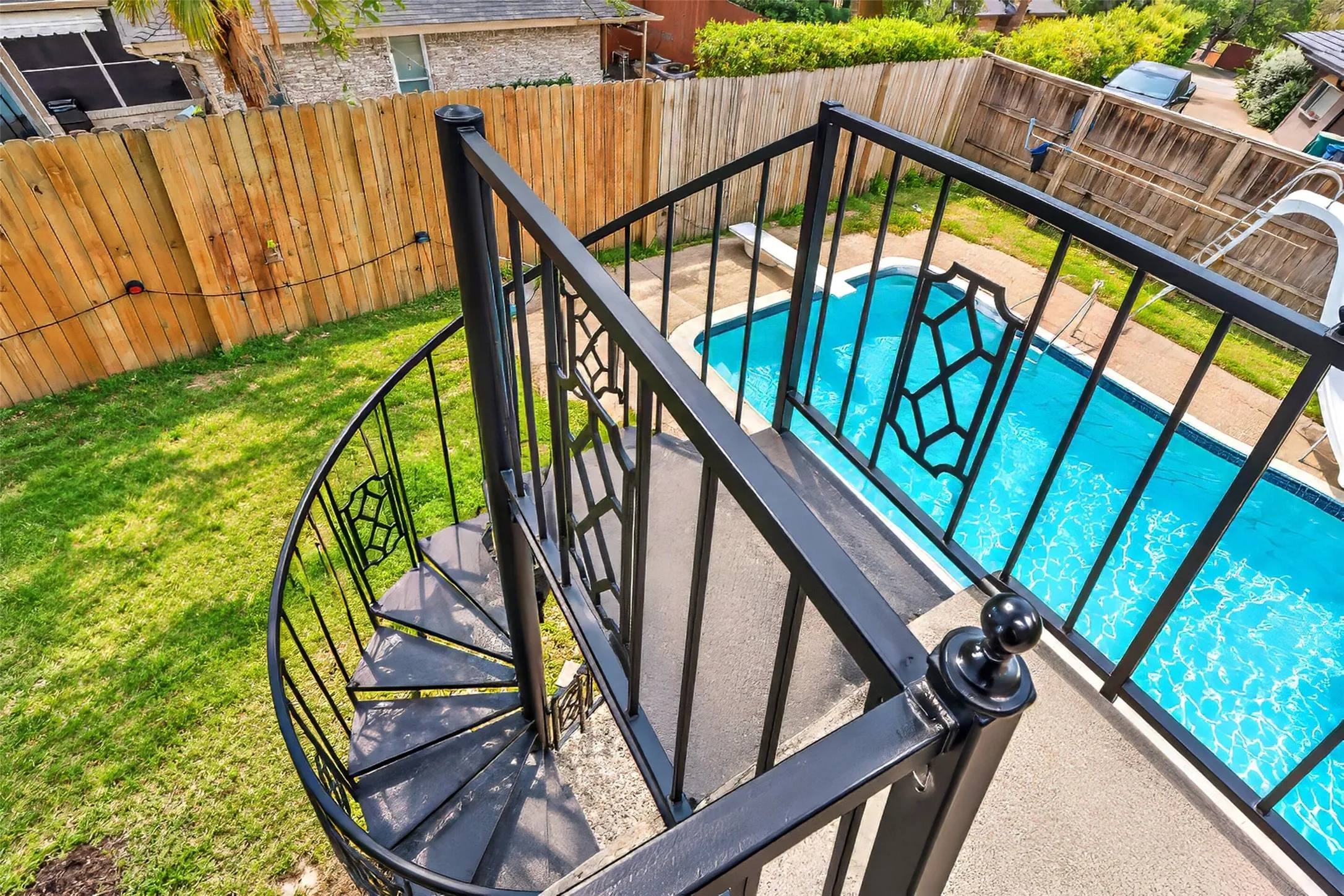 Black metal spiral staircase with decorative railings and a rectangular swimming pool