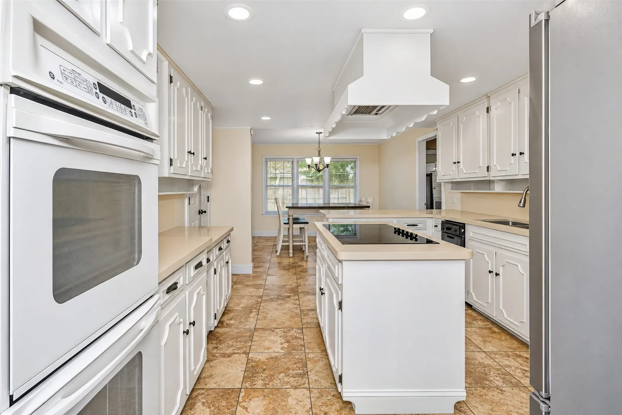 Kitchen featuring white cabinetry, light countertops, tile flooring, built-in oven, and a center island with a cooktop