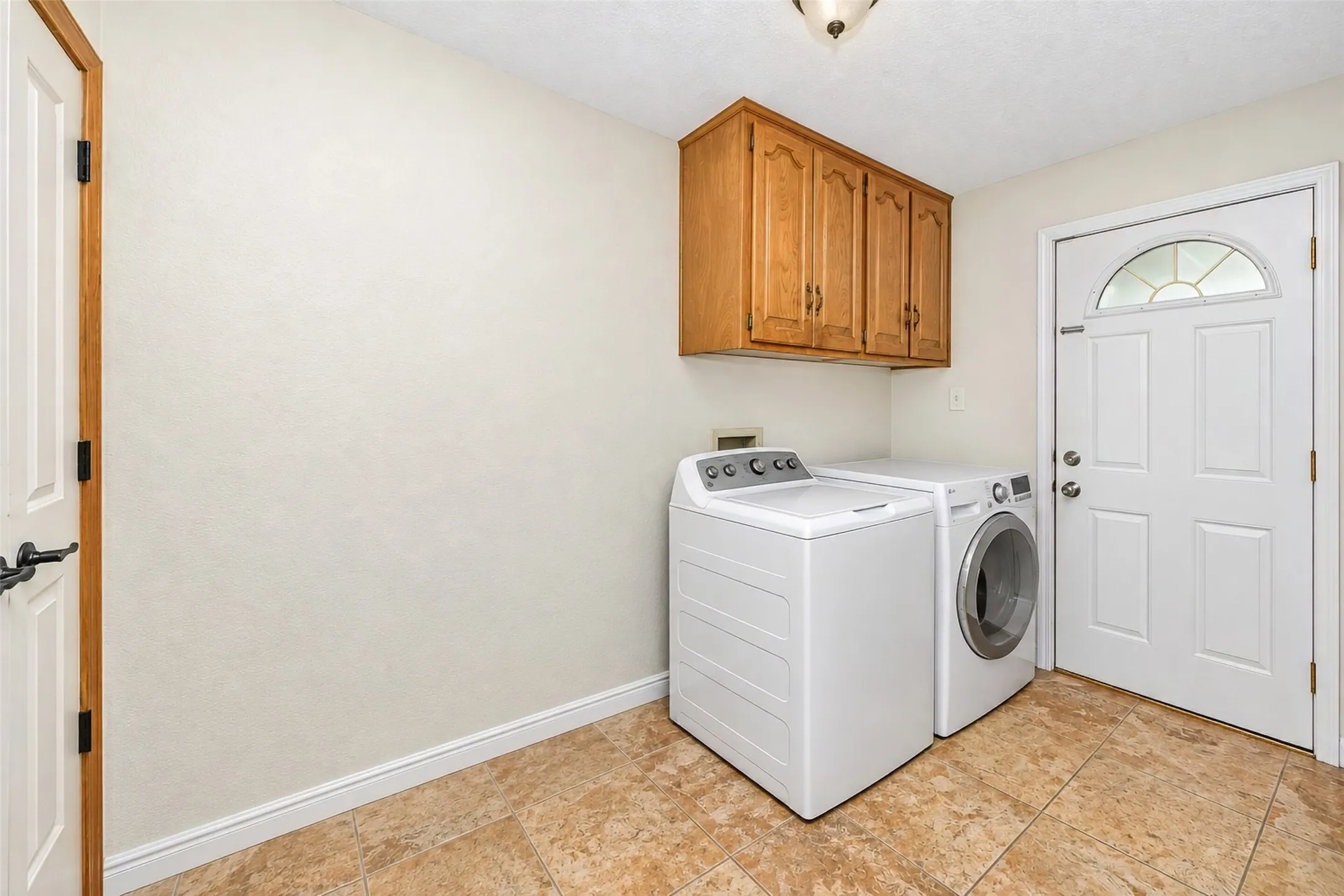 Laundry area with wood-finish cabinetry, tile flooring, and a paneled exterior door with an arched glass insert
