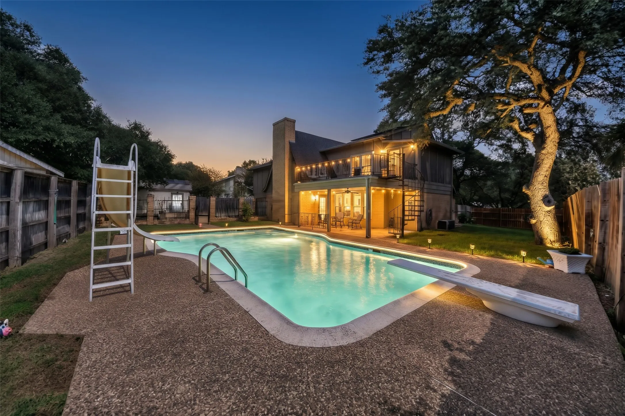 Expansive backyard featuring a concrete patio, built-in swimming pool, diving board, and mature trees
