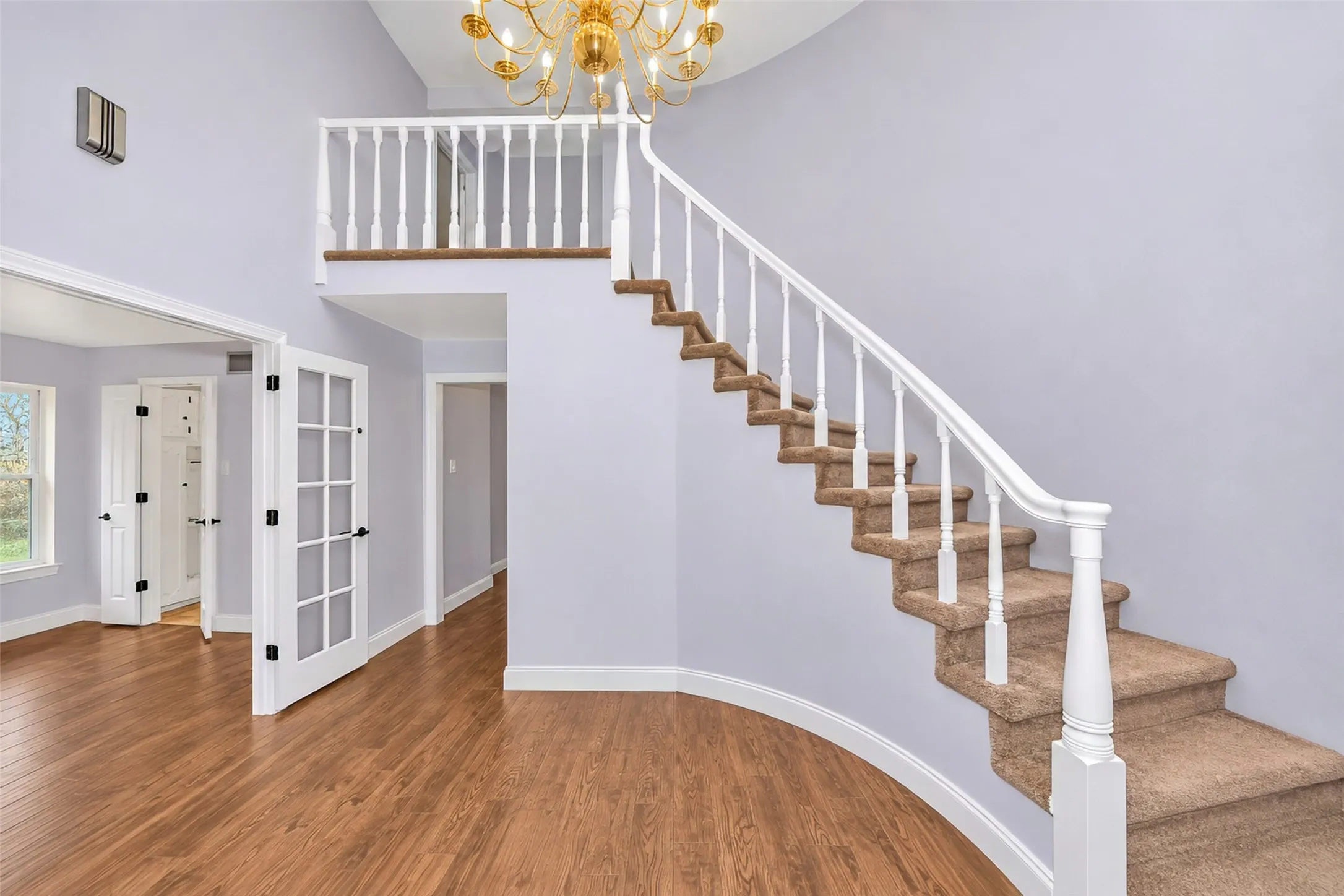 Double French doors, wood-finish flooring, staircase with carpeted treads, white balusters, and an ornate chandelier
