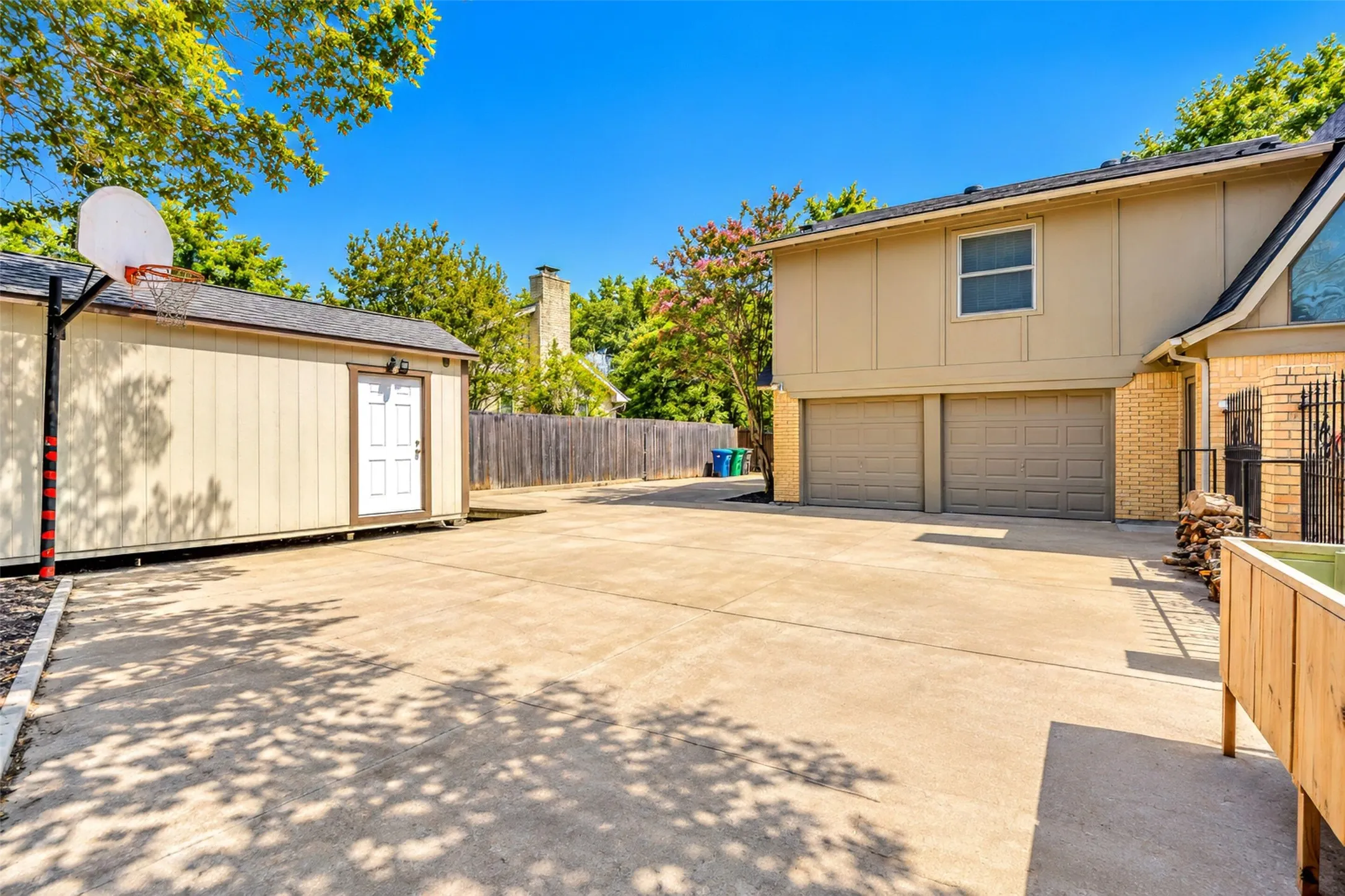 Expansive concrete driveway, attached two-car garage, separate storage shed, and durable wood fence