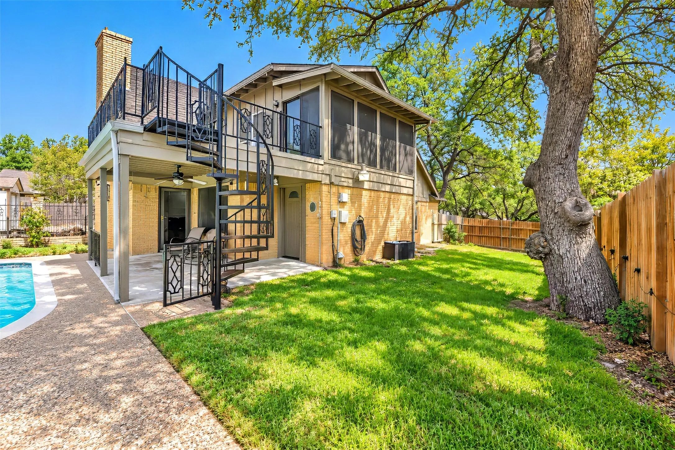 Expansive backyard featuring a manicured lawn, an in-ground swimming pool with surrounding hardscaping, a covered patio area, and a spiral staircase leading to an upper-level balcony