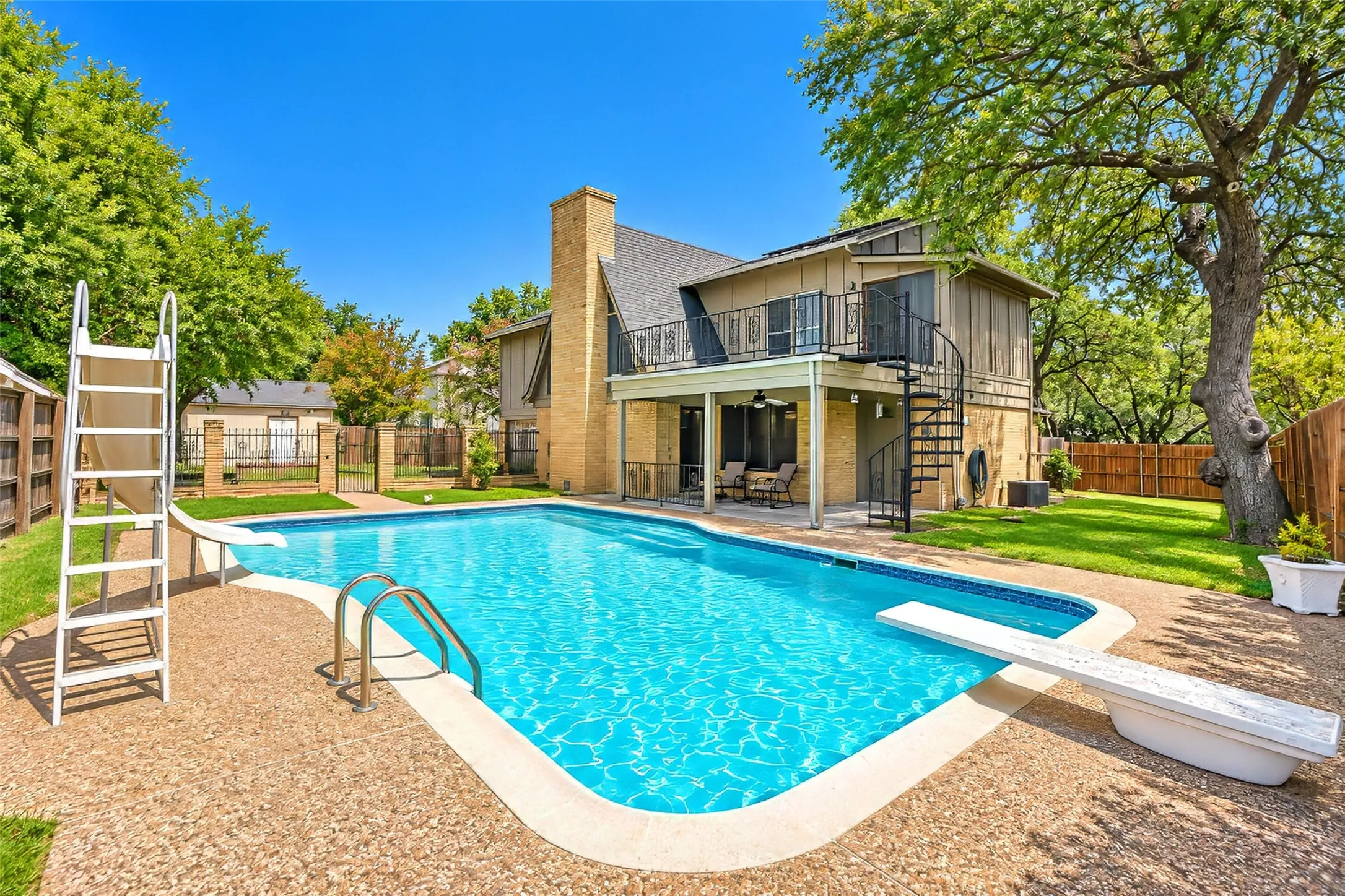 Expansive backyard featuring a swimming pool, diving board, and a covered patio