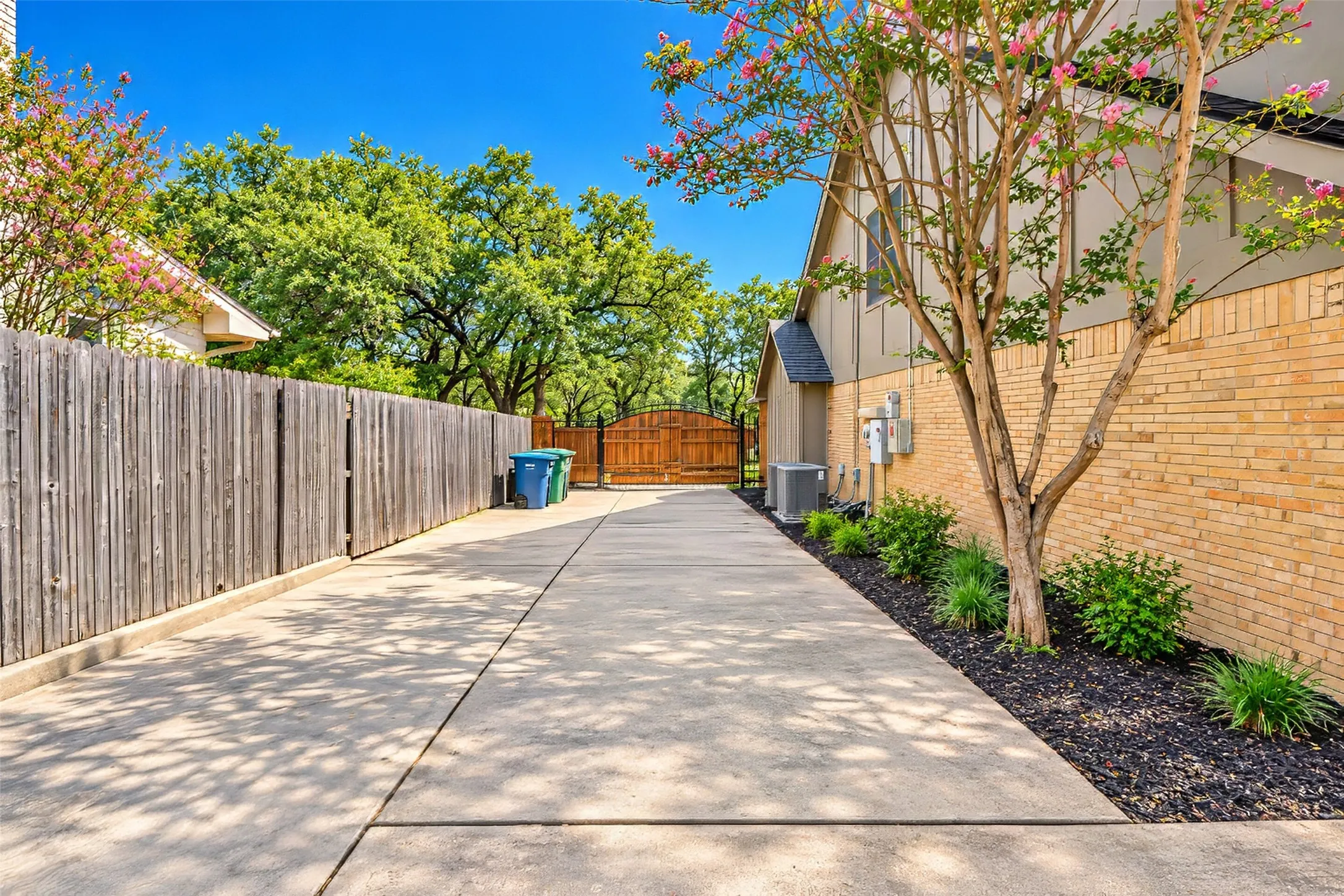 Expansive concrete driveway bordered by a tall wooden fence and mature trees