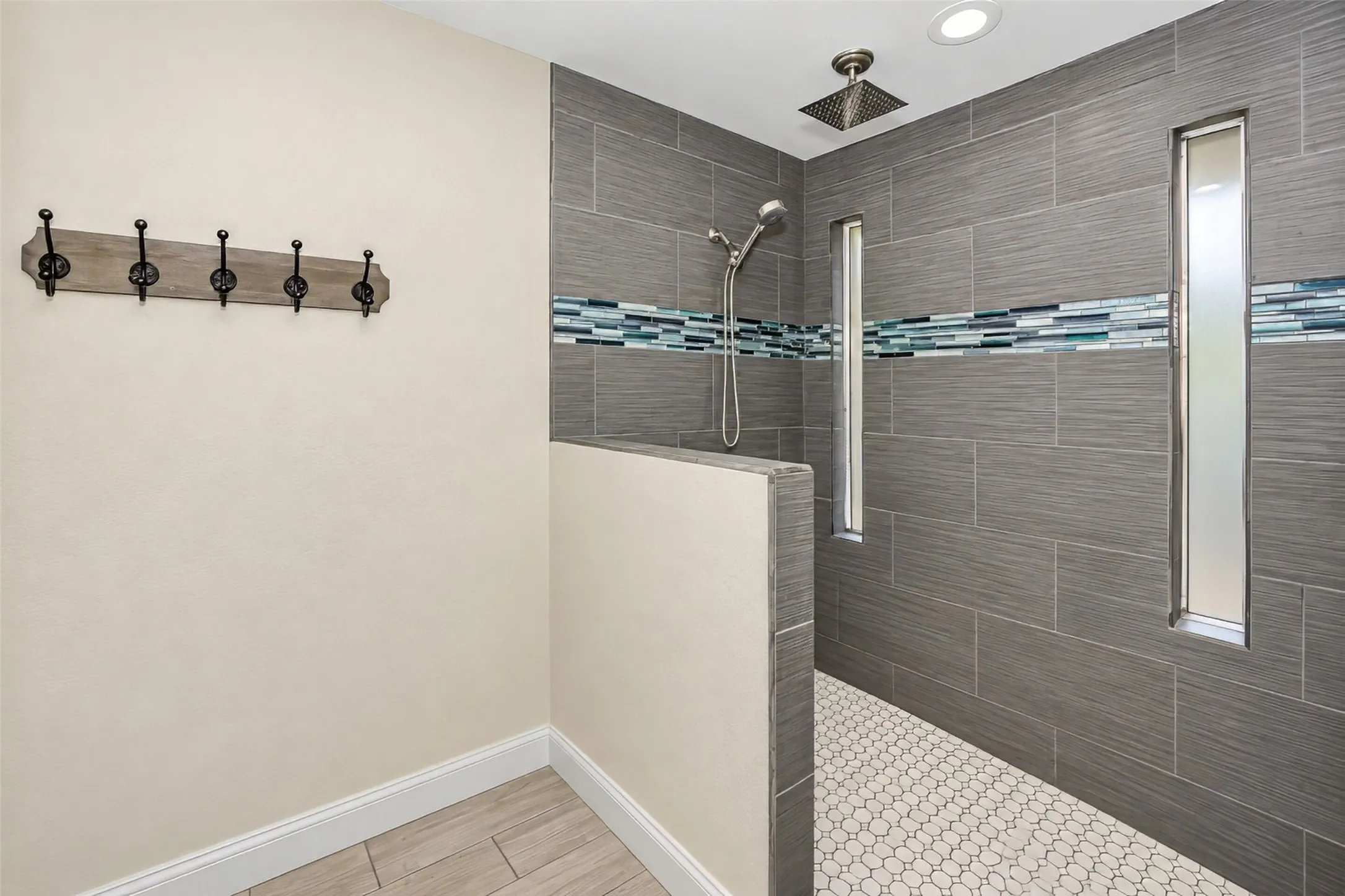 Walk-in shower with gray tile surround, decorative mosaic accent band, and a hexagonal tile floor