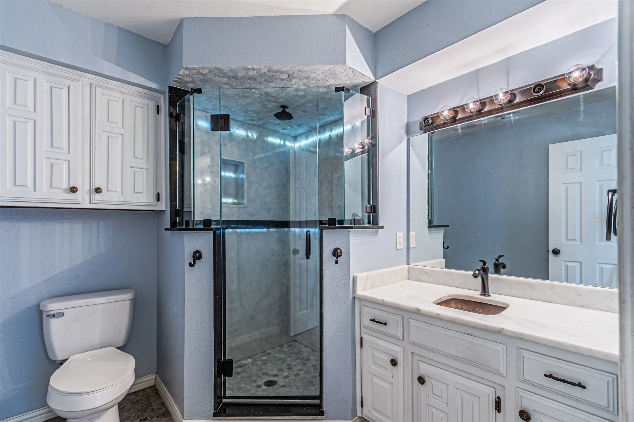 Glass-enclosed shower with a rainfall showerhead, vanity with an integrated sink, broad wall mirror, and white shaker-style cabinetry