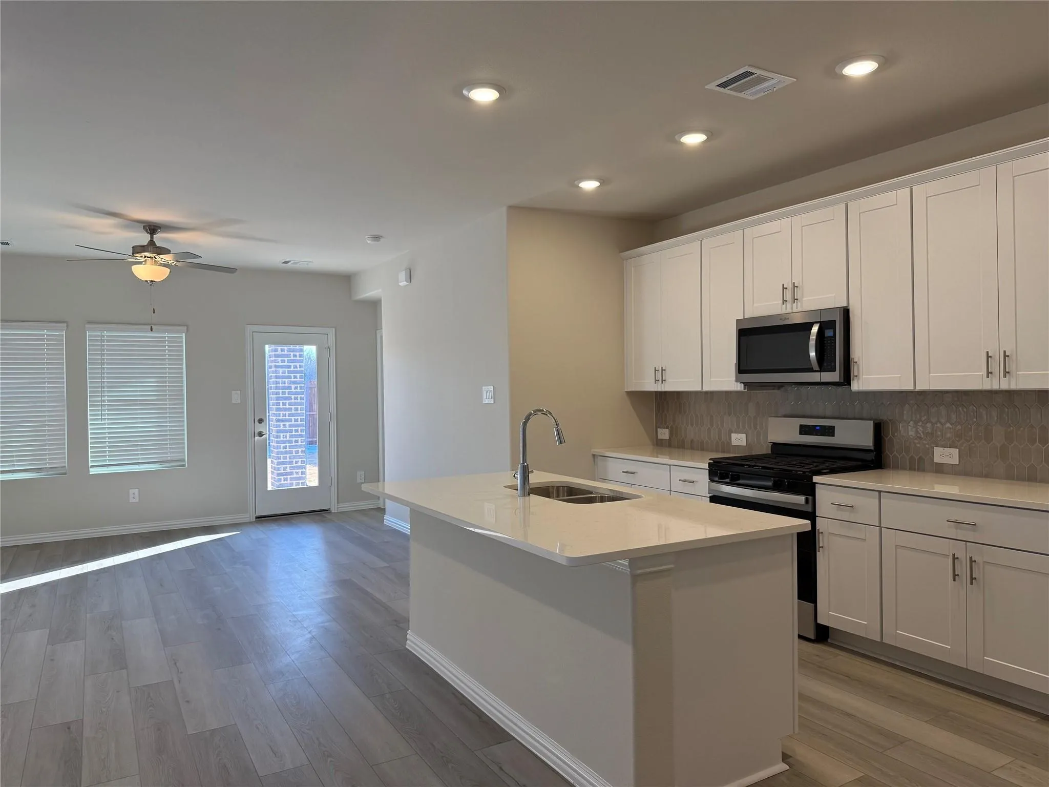 Open-concept kitchen with white shaker cabinetry, stainless steel appliances, and a central island with an undermount sink