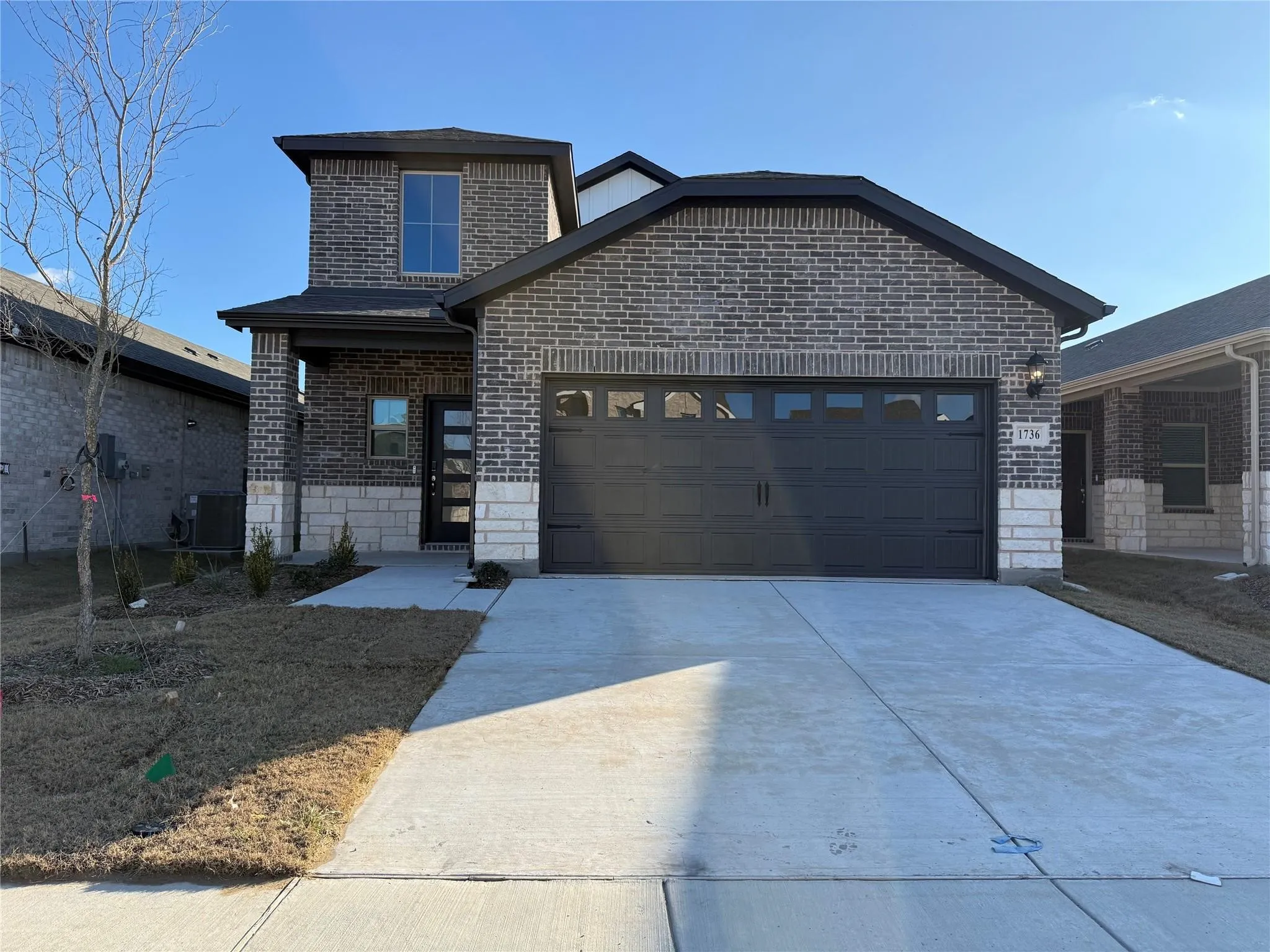 Brick and stone exterior with a covered porch entry, a multi-pane front door, and a two-car garage with windows