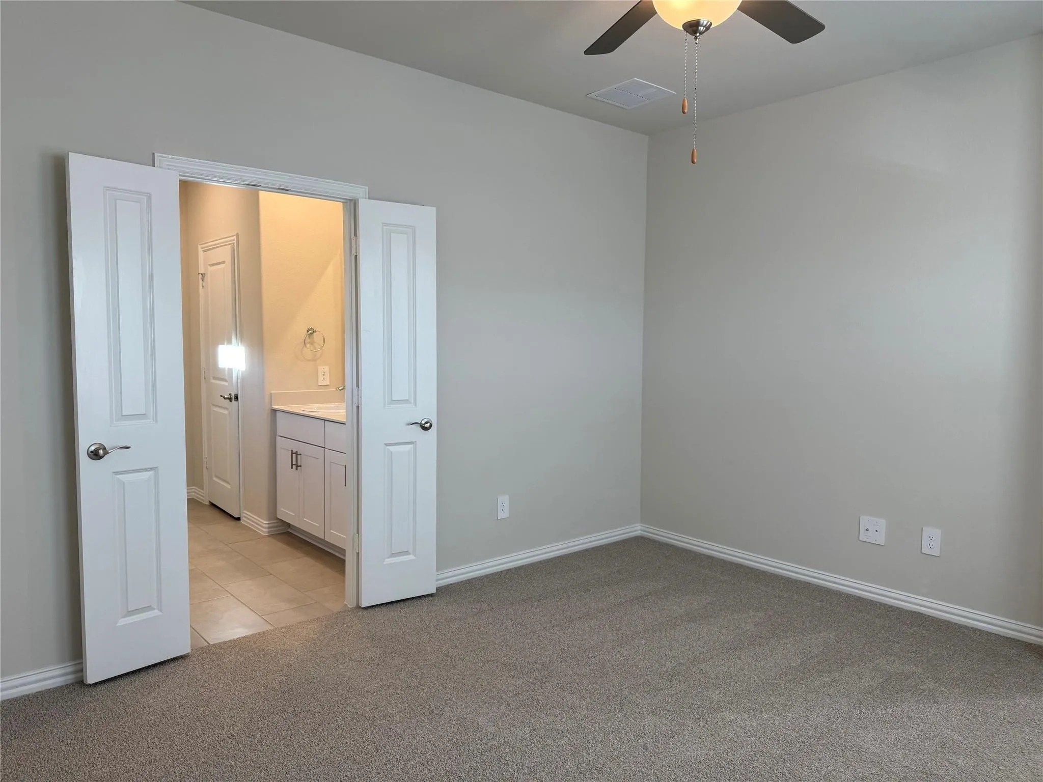 Neutral tone wall paint, flush mount ceiling fan, carpeted flooring, white paneled doors, and a bathroom vanity with a countertop
