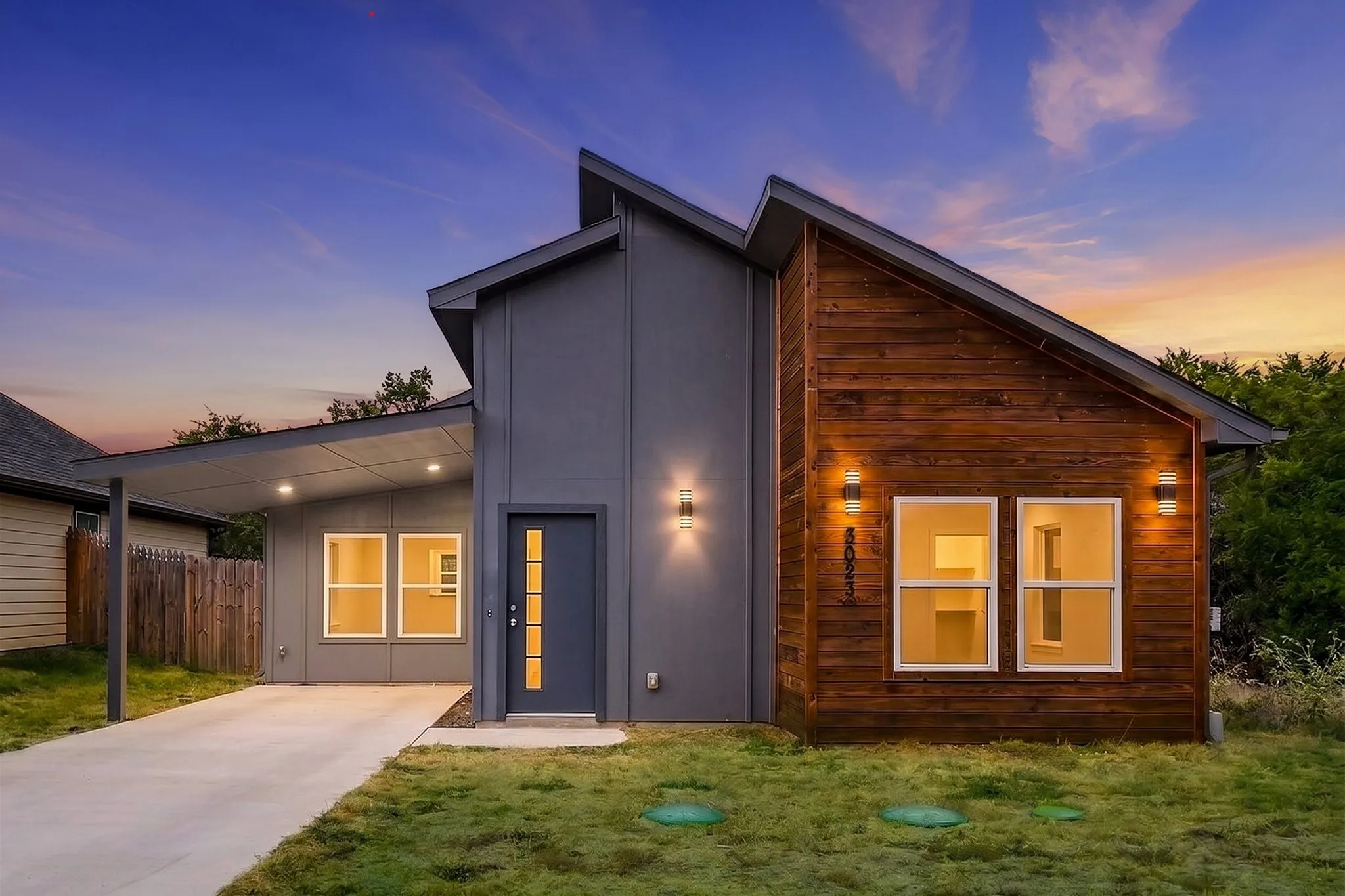 Modern exterior with a contrasting wood panel accent, gray siding, a covered entry, and a covered carport