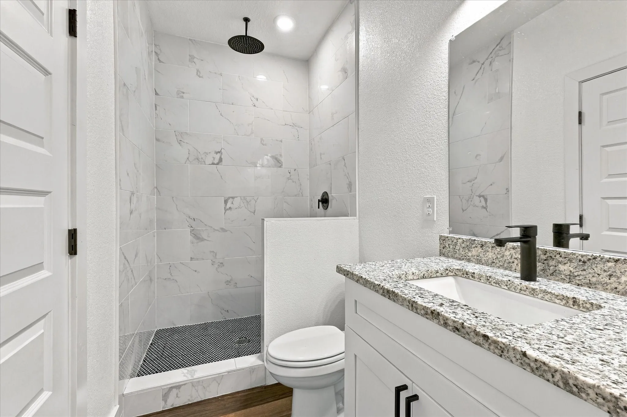 Walk-in shower with ceiling-mounted rain showerhead, white marble-style tiled walls, and dark tiled floor