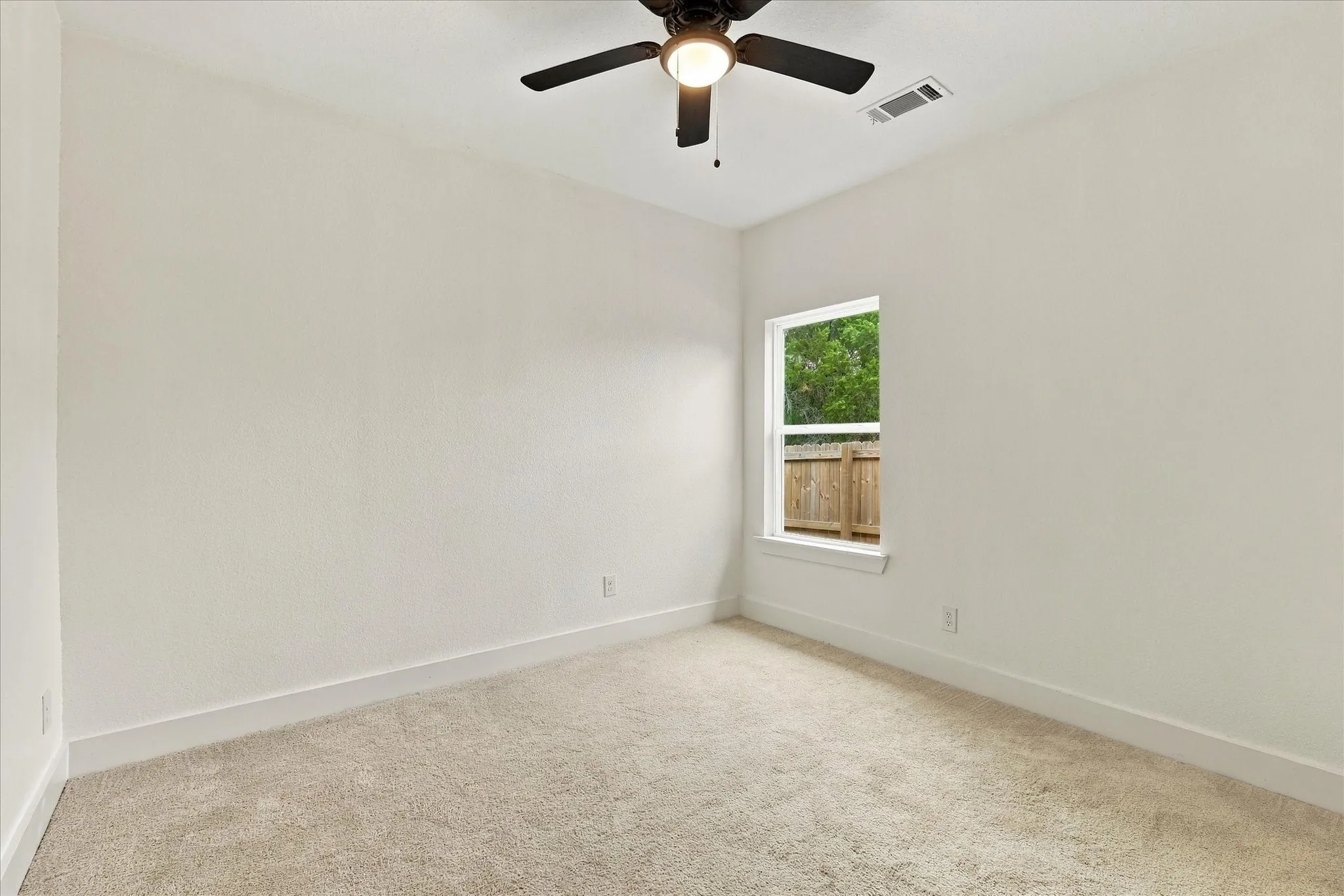 Neutral-toned carpeting, white walls, a single window, and a ceiling fan with integrated lighting