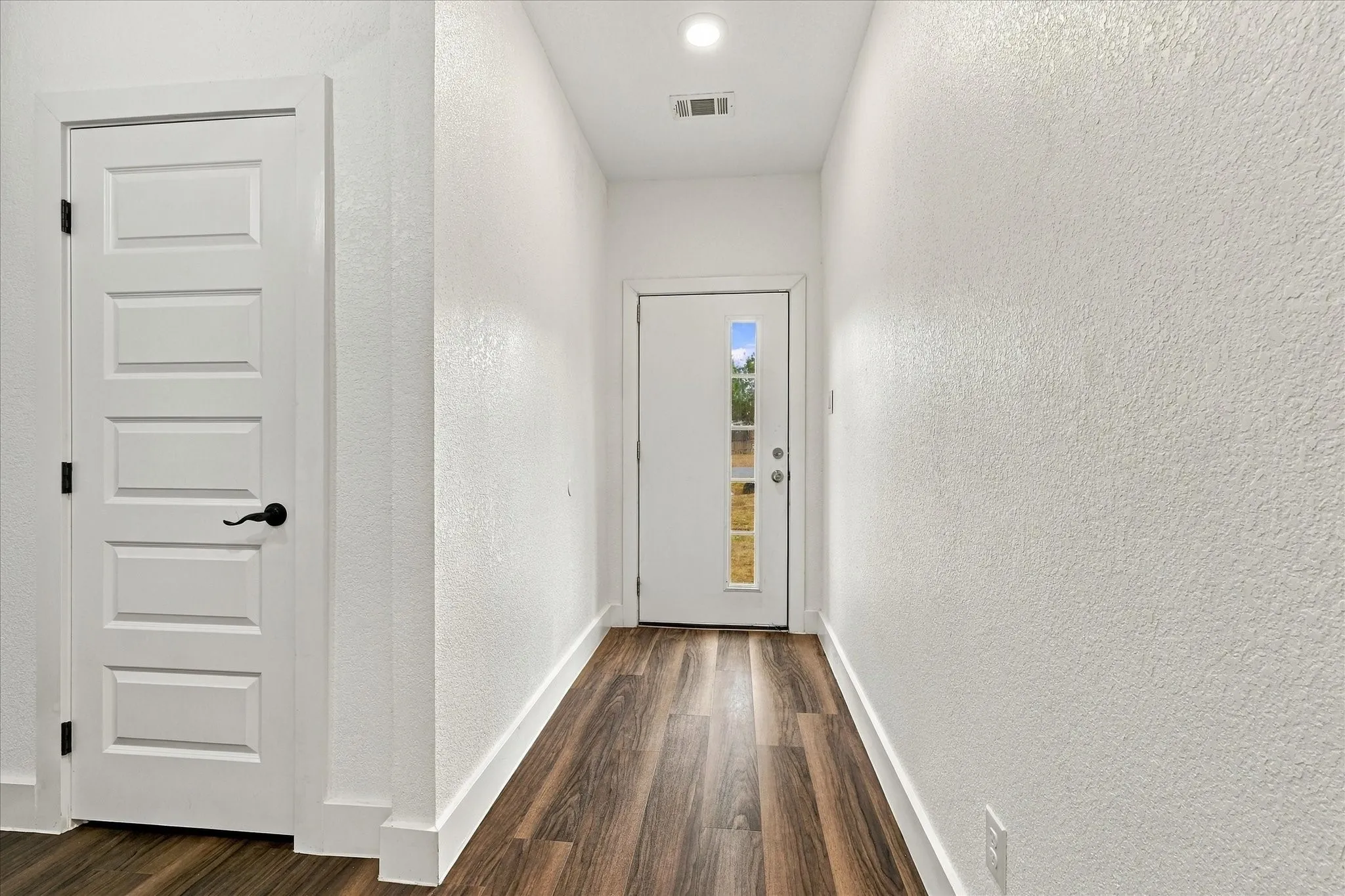 Wood-finish flooring, white paneled interior doors with black hardware, recessed lighting, and a front entry door with vertical window panels