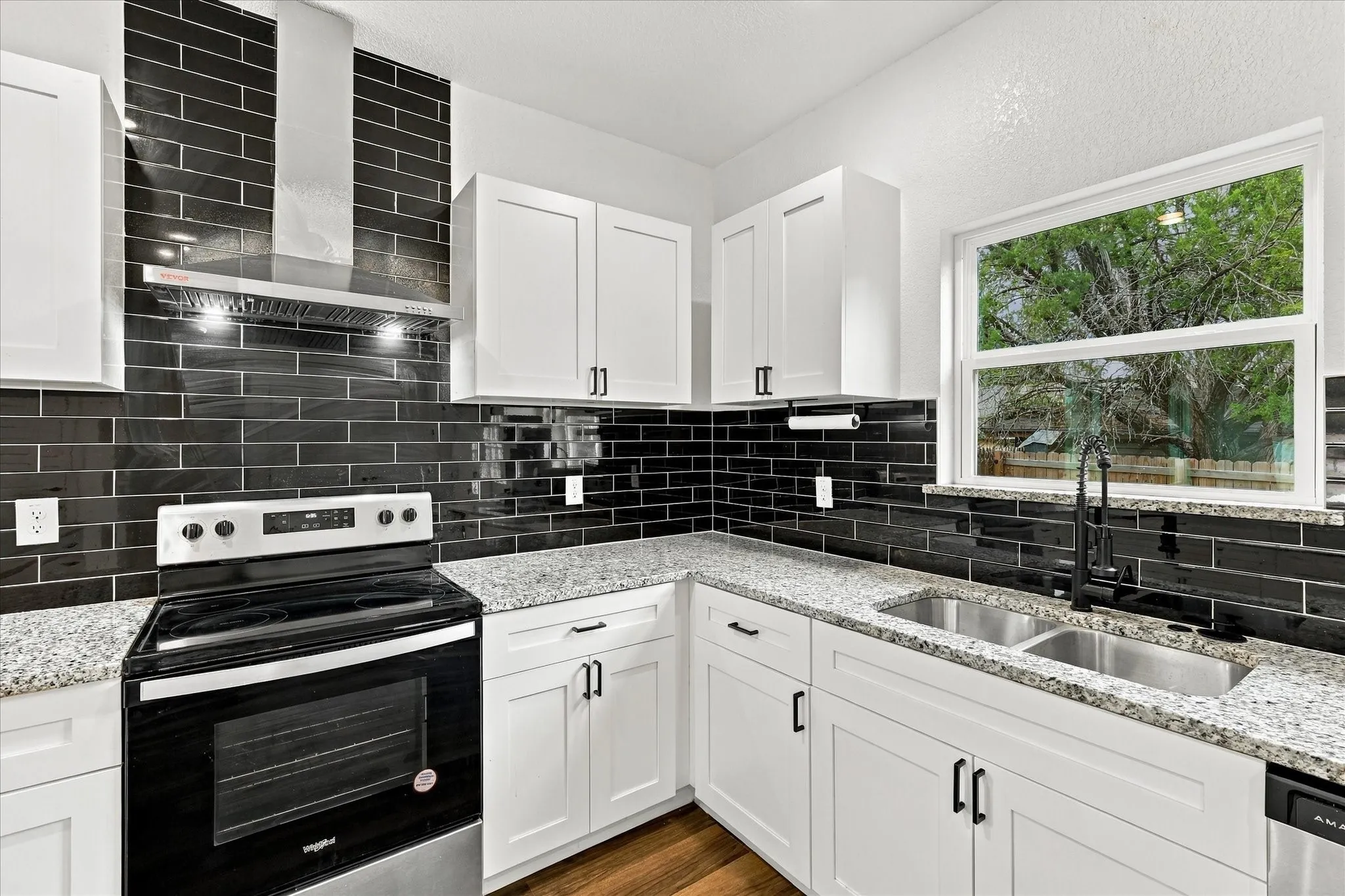 Modern kitchen featuring white shaker cabinetry, granite countertops, a black subway tile backsplash, stainless steel appliances, and a double basin sink with a black faucet