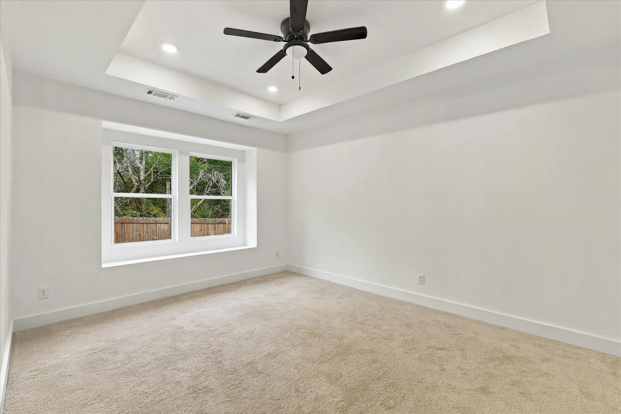 Tray ceiling with recessed lighting, ceiling fan, carpeting, and a double window