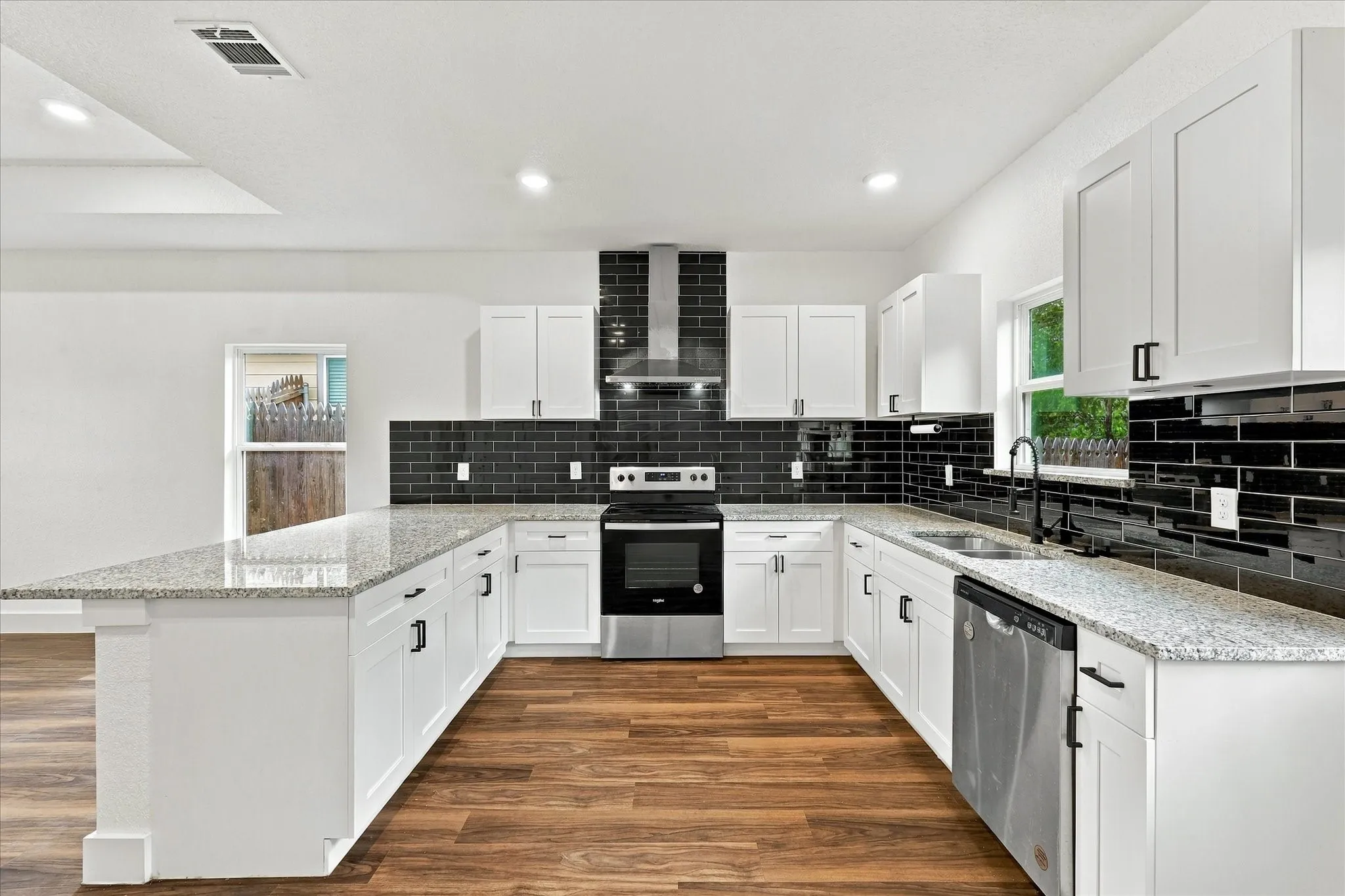 Kitchen featuring white shaker cabinetry, light-toned countertops, a black subway tile backsplash, stainless steel appliances, and wood-finish flooring