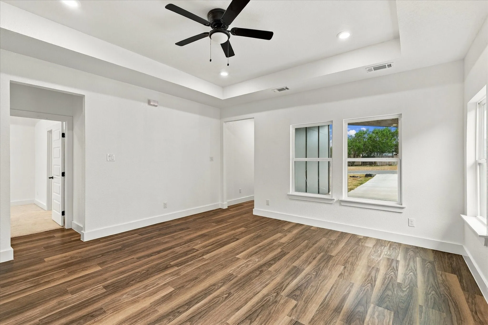 Wood-finish flooring, recessed lighting, ceiling fan, and tray ceiling detail