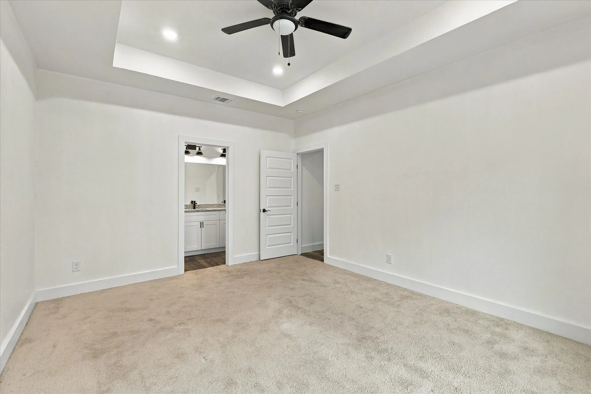 Tray ceiling with recessed lighting, ceiling fan, and light-toned carpet flooring