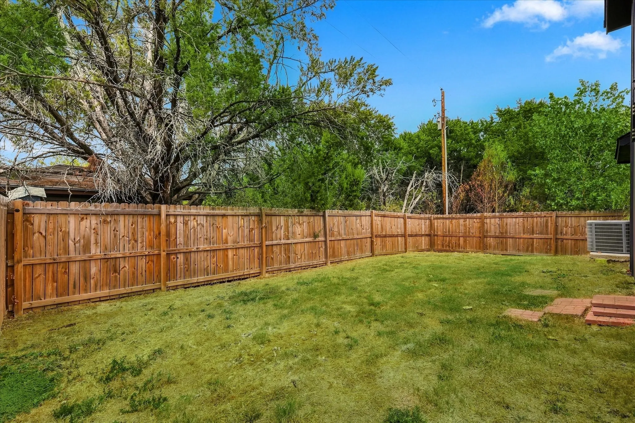 Expansive fenced backyard with a grassy lawn, mature trees, and brick paver steps